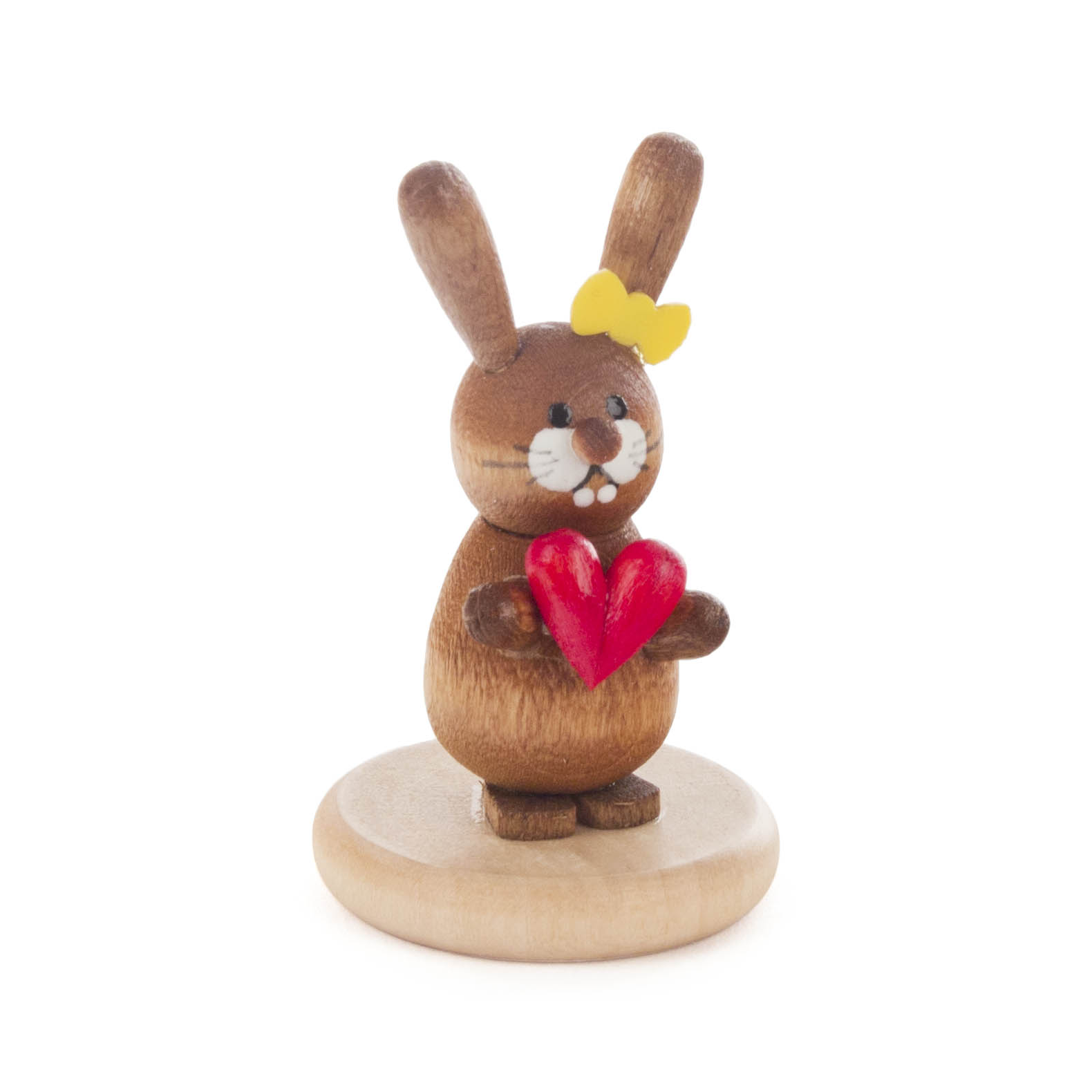 Lächelnder, brauner Holz-Hase mit gelber Schleife, hält rotes Herz. Steht auf rundem, holzfarbenem Sockel. Figur ist handgefertigt und lasiert. im Dregeno Online Shop günstig kaufen