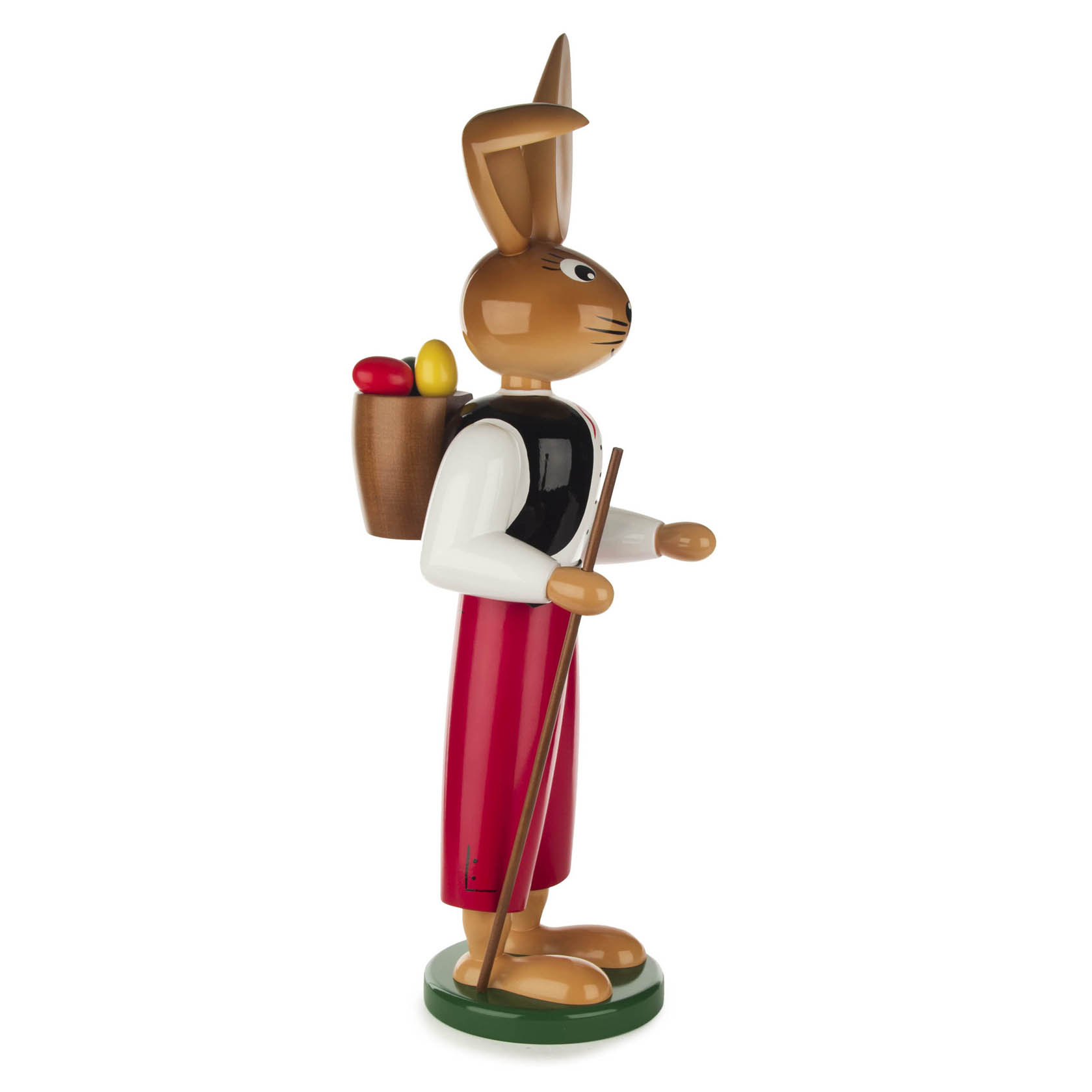 Holzfigur eines Hasen mit roten Hosen, weißem Hemd und schwarzer Weste. Der Hase trägt einen Rucksack mit Eiern und hält einen Stab in der Pfote.