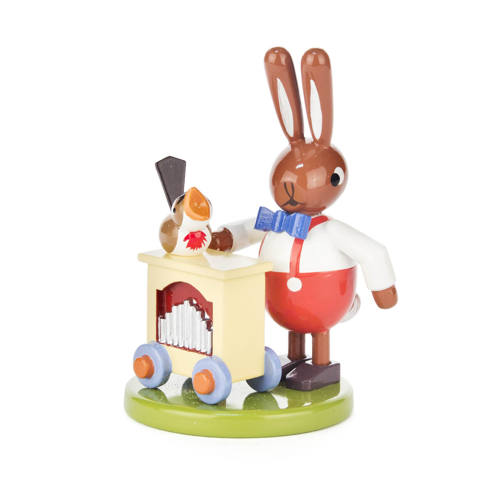 Ein hölzerner Hase mit einer blauen Fliege und roter Hose steht neben einem kleinen, gelben Leierkasten auf Rädern und einer Holzfigur eines Vogels. im Dregeno Online Shop günstig kaufen