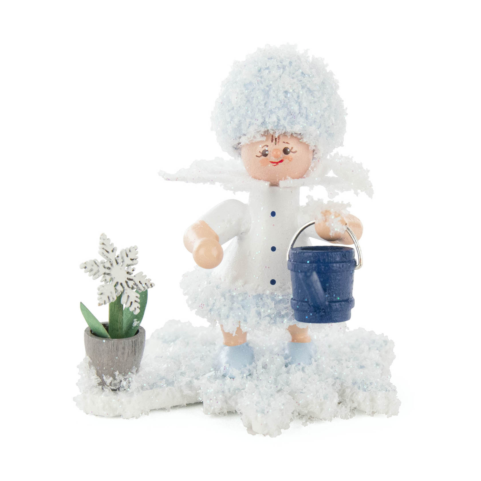 Eine Schneefigur in Form eines Mädchens mit einem pelzigen Hut, das eine kleine blaue Gießkanne hält und neben einem Topf mit einer Schneeflockenpflanze steht. im Dregeno Online Shop günstig kaufen