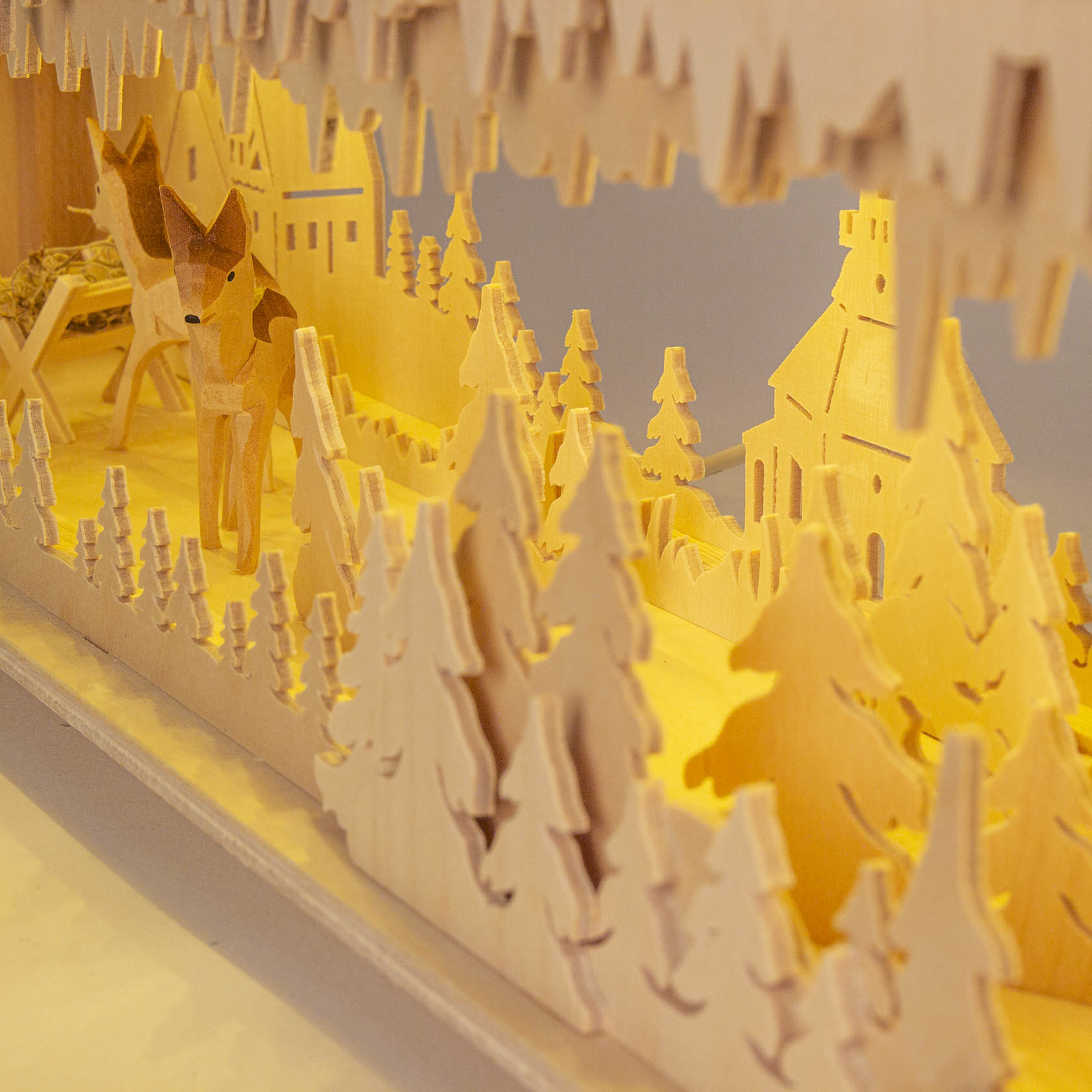 Wooden LED base light depicting a forest scene with deer and a nativity, set in a laser-cut arch with warm lighting.