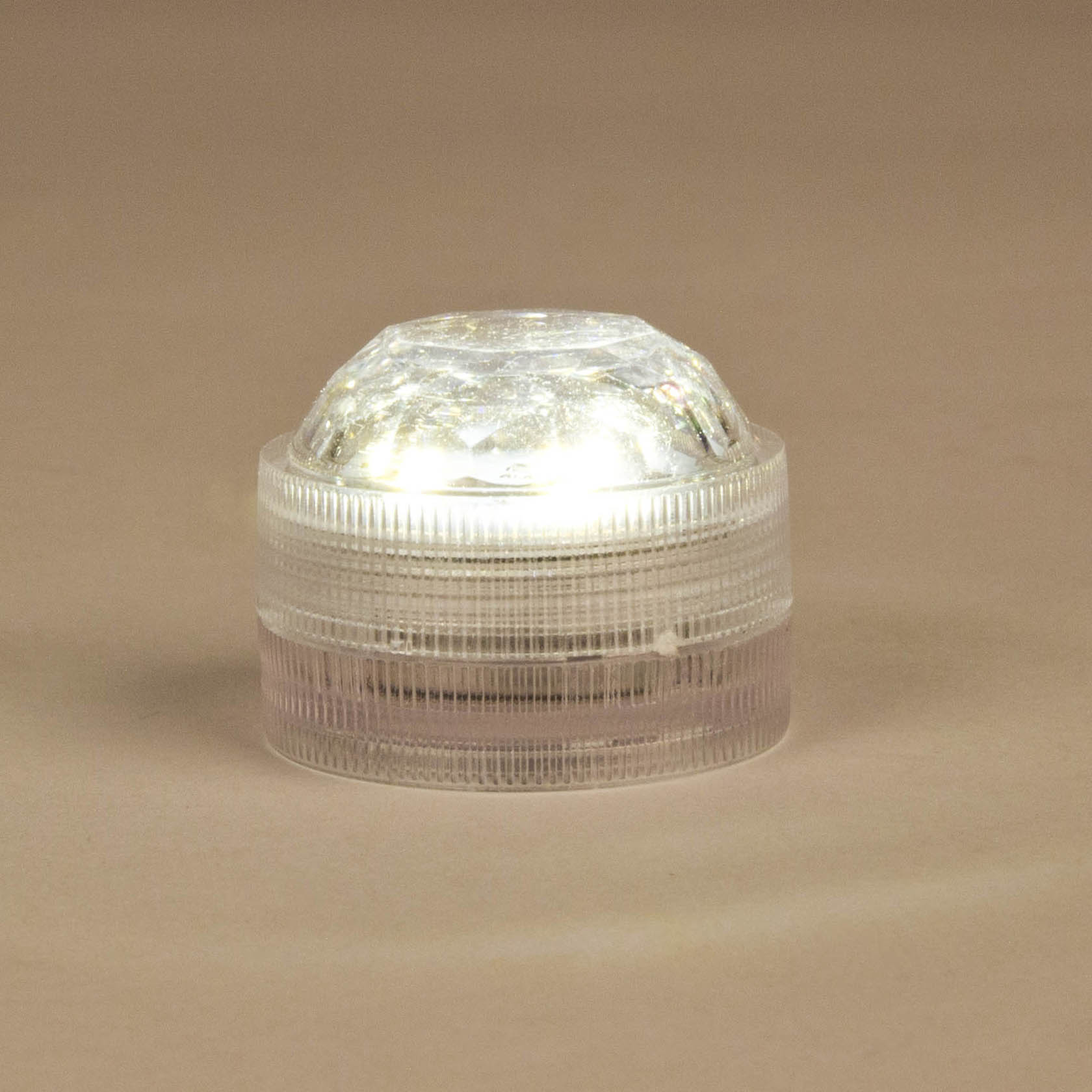 Transparente runde LED-Dekoleuchte mit texturiertem Gehäuse und leuchtendem Licht auf braunem Hintergrund.