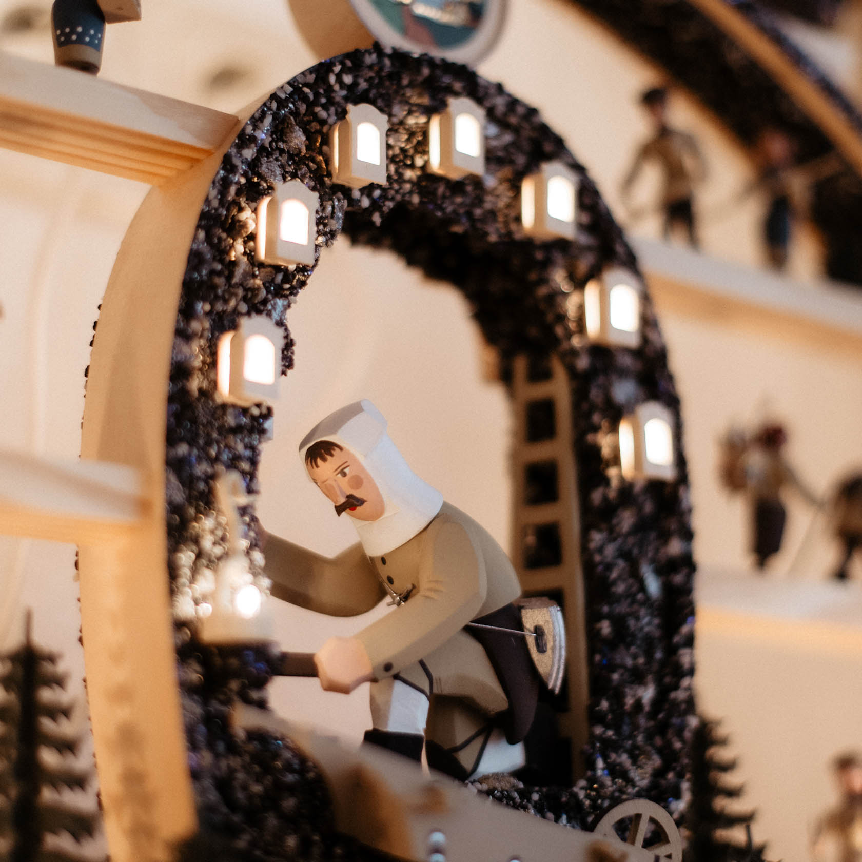 A wooden arch display shows a miner figure holding a lamp, surrounded by small lanterns on a carved arch, symbolizing a mining scene.