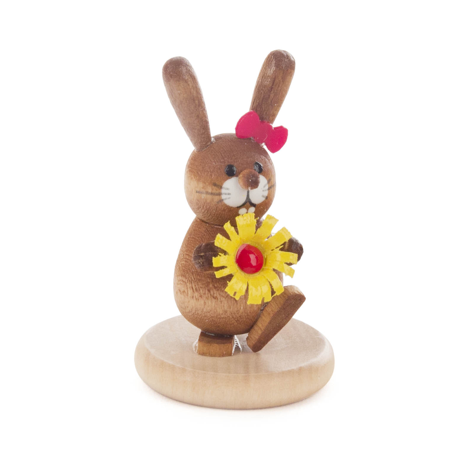 Eine bunte, lasierte Holzfigur eines Hasen mit roter Schleife und gelber Blume, stehend auf einem runden Holzsockel. im Dregeno Online Shop günstig kaufen