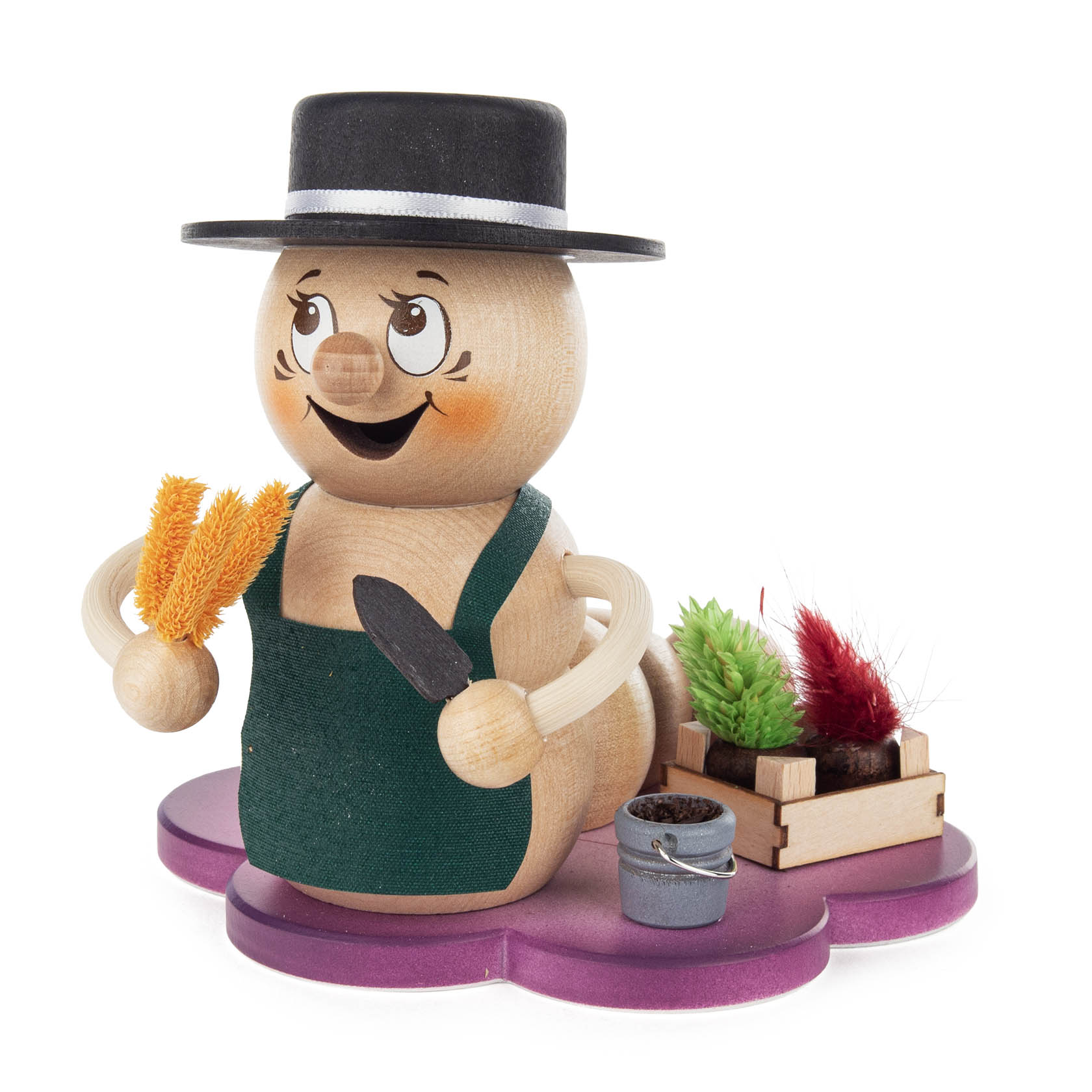Ein lächelnder, hölzerner Räucherwurm namens Rudi Gärtner trägt eine grüne Schürze und einen schwarzen Hut, hält Gartenwerkzeuge und ist von Pflanzen umgeben. im Dregeno Online Shop günstig kaufen