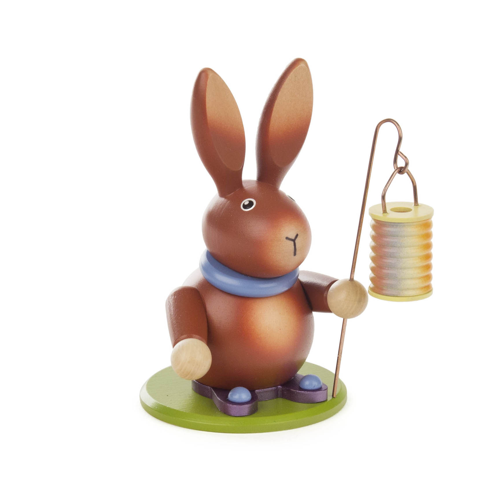 Ein Holzhasenfigur, die einen Lampion auf einem Stab hält, steht auf einem grünen Sockel. Der Hase trägt ein blaues Halstuch. im Dregeno Online Shop günstig kaufen