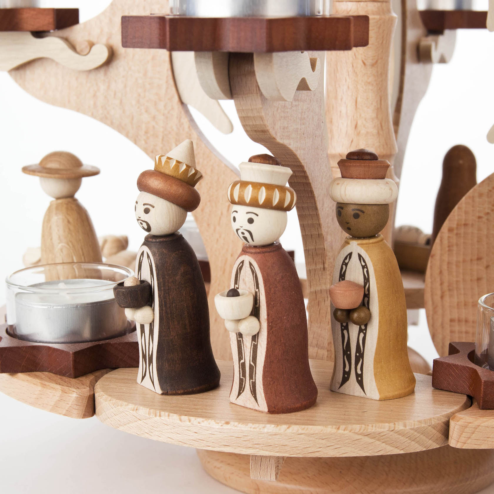 Drei handgeschnitzte, bunt bemalte Holzfiguren der Heiligen Drei Könige auf einem hölzernen Weihnachtskranz für Teelichte, der Szenen der Geburt Christi darstellt.