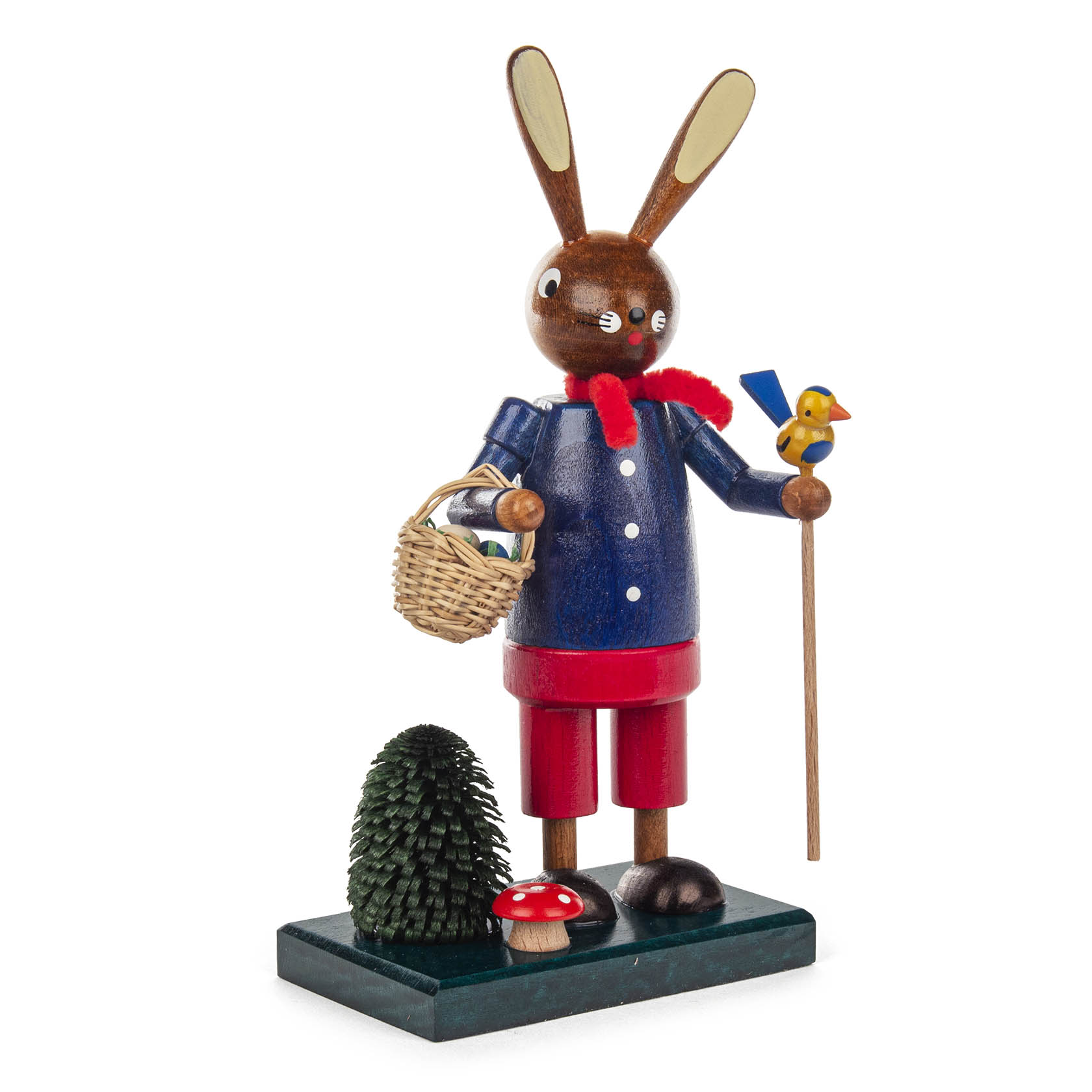 Holzfigur eines Osterhasen mit blauer Jacke und rotem Schal, hält einen Stock mit gelbem Küken und Korb, steht neben kleinem Baum und Pilz.