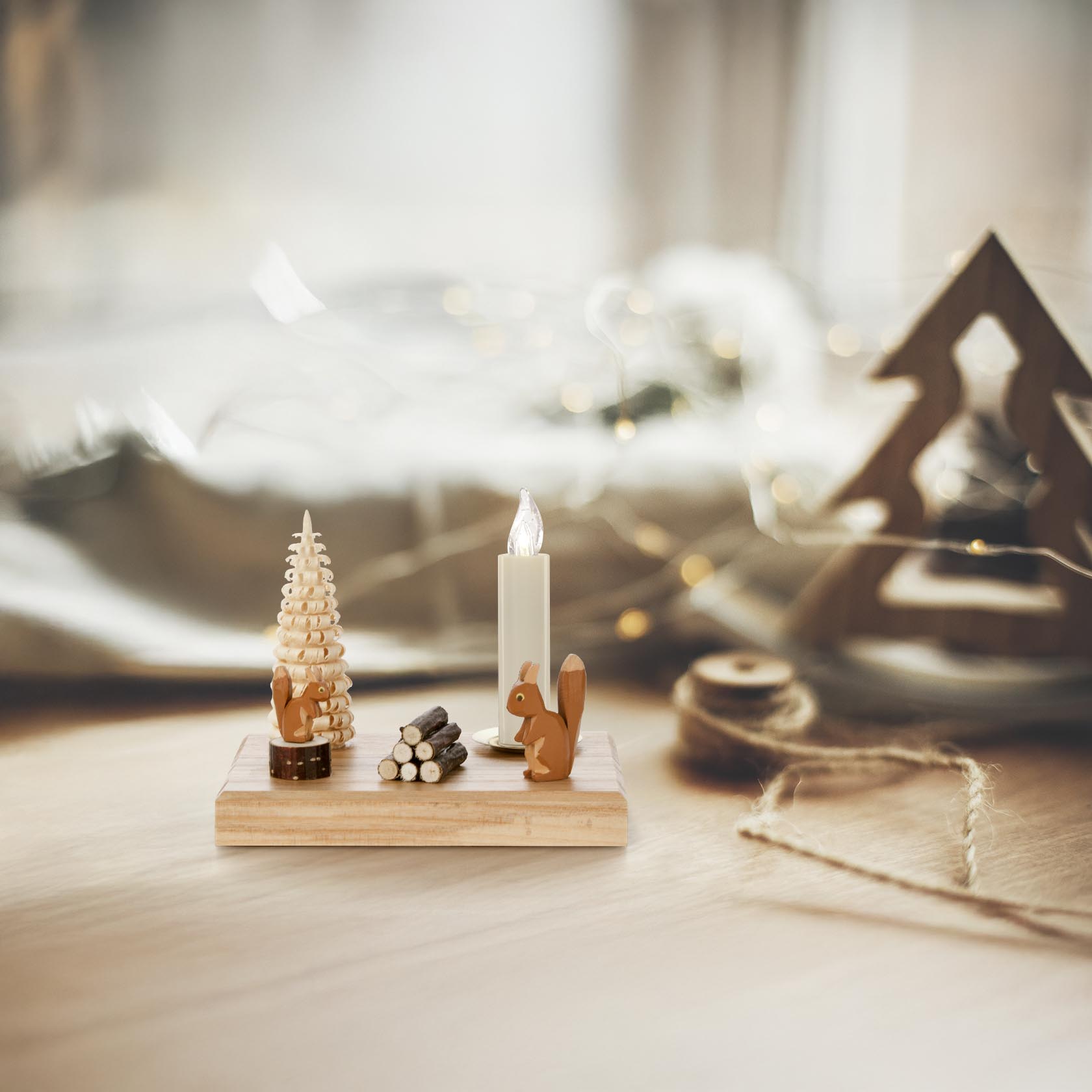 Ein dekorativer Kerzenhalter auf einem Holzboden. Es zeigt ein Eichhörnchen neben einem kunstvollen Holztannenbaum und einem Bündel Miniholzstapel. Der Halter ist für eine Kerze mit 14 mm Durchmesser geeignet.