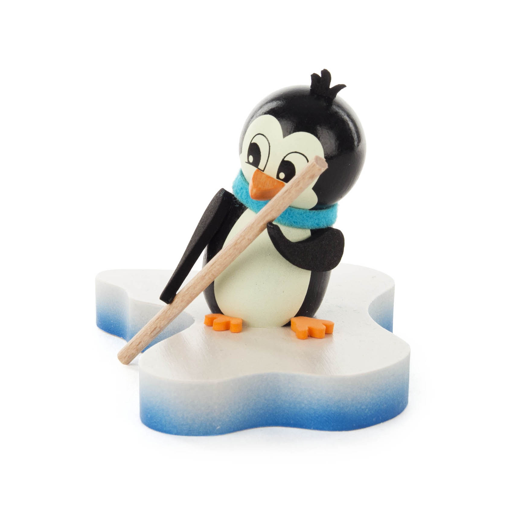 Kleiner Pinguin aus Holz, trägt einen blauen Schal und hält einen Stock auf einer schneeflockenförmigen Basis.