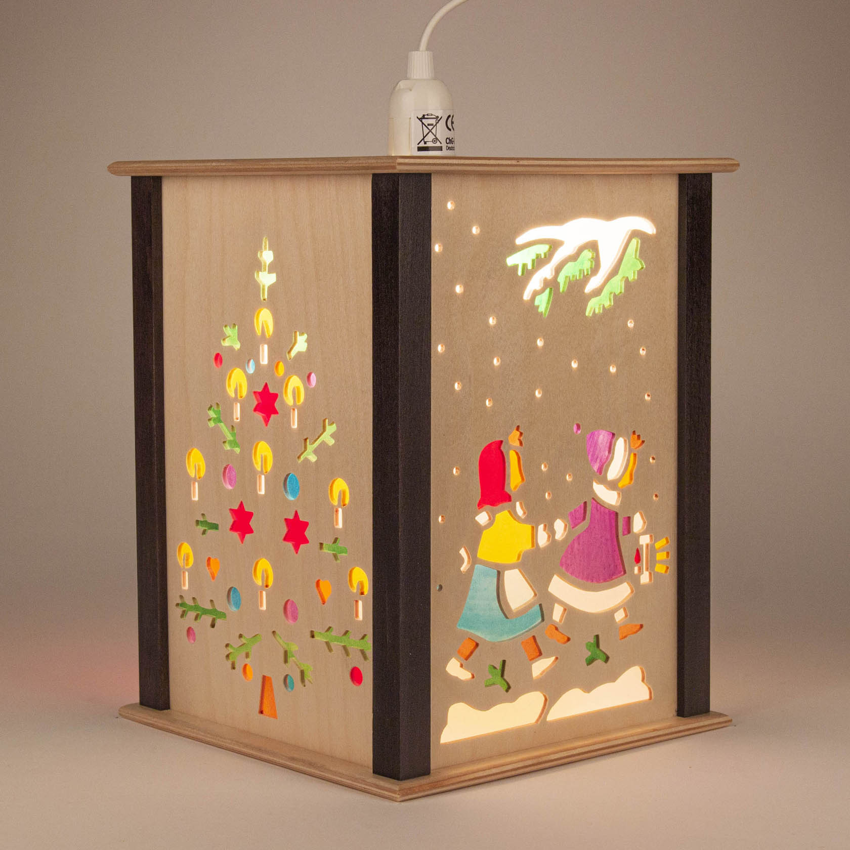 Holzlaterne mit zwei Seiten, eine zeigt bunte Weihnachtsbaum, andere zwei Kinder im Schnee, eines mit Päckchen, beide mit Mütze.