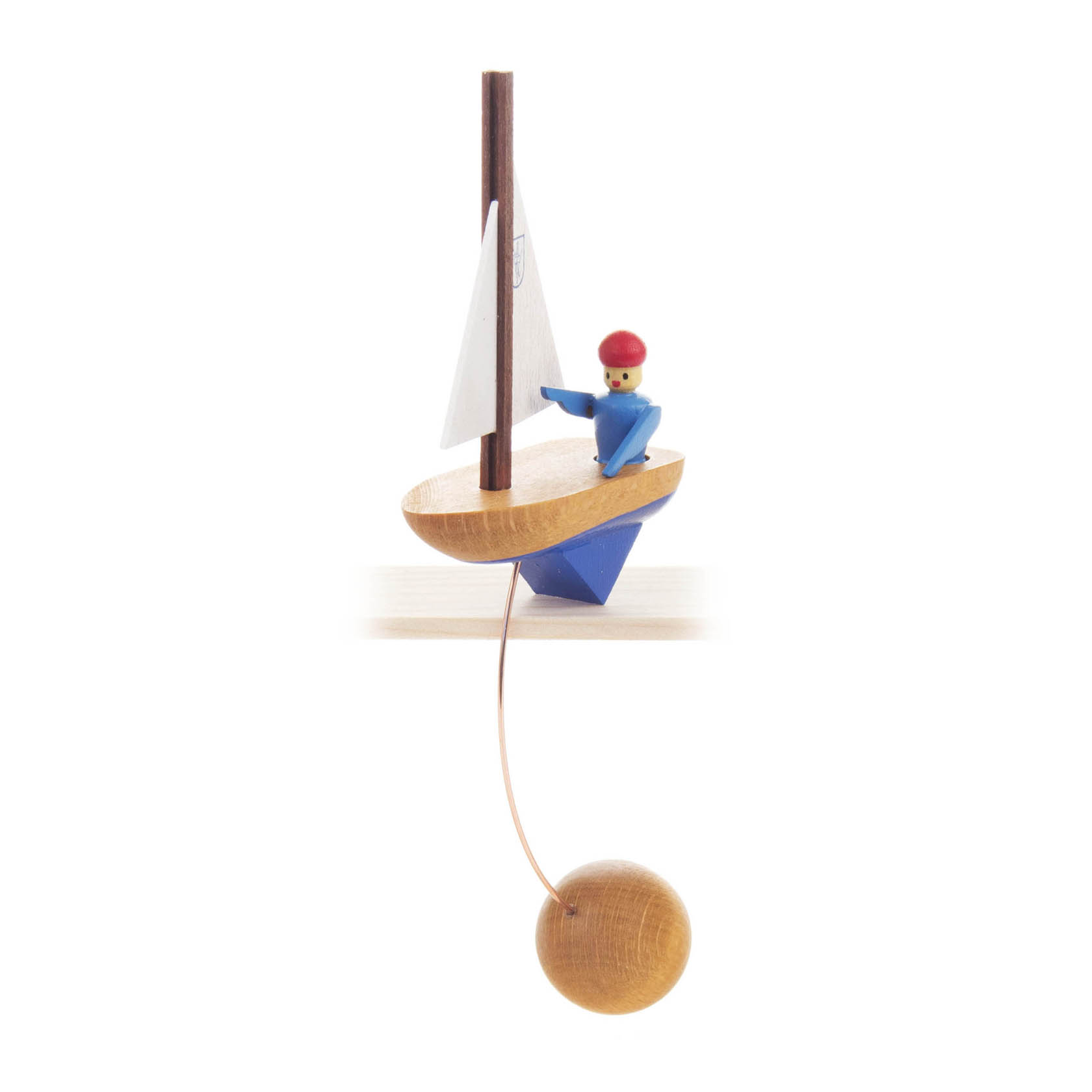 Holzspielzeug-Segelschiff mit kleinem blauen Matrosen mit roter Mütze, der auf dem Deck steht. Unterhalb des Schiffs hängt eine Holzkugel an einem Draht. im Dregeno Online Shop günstig kaufen