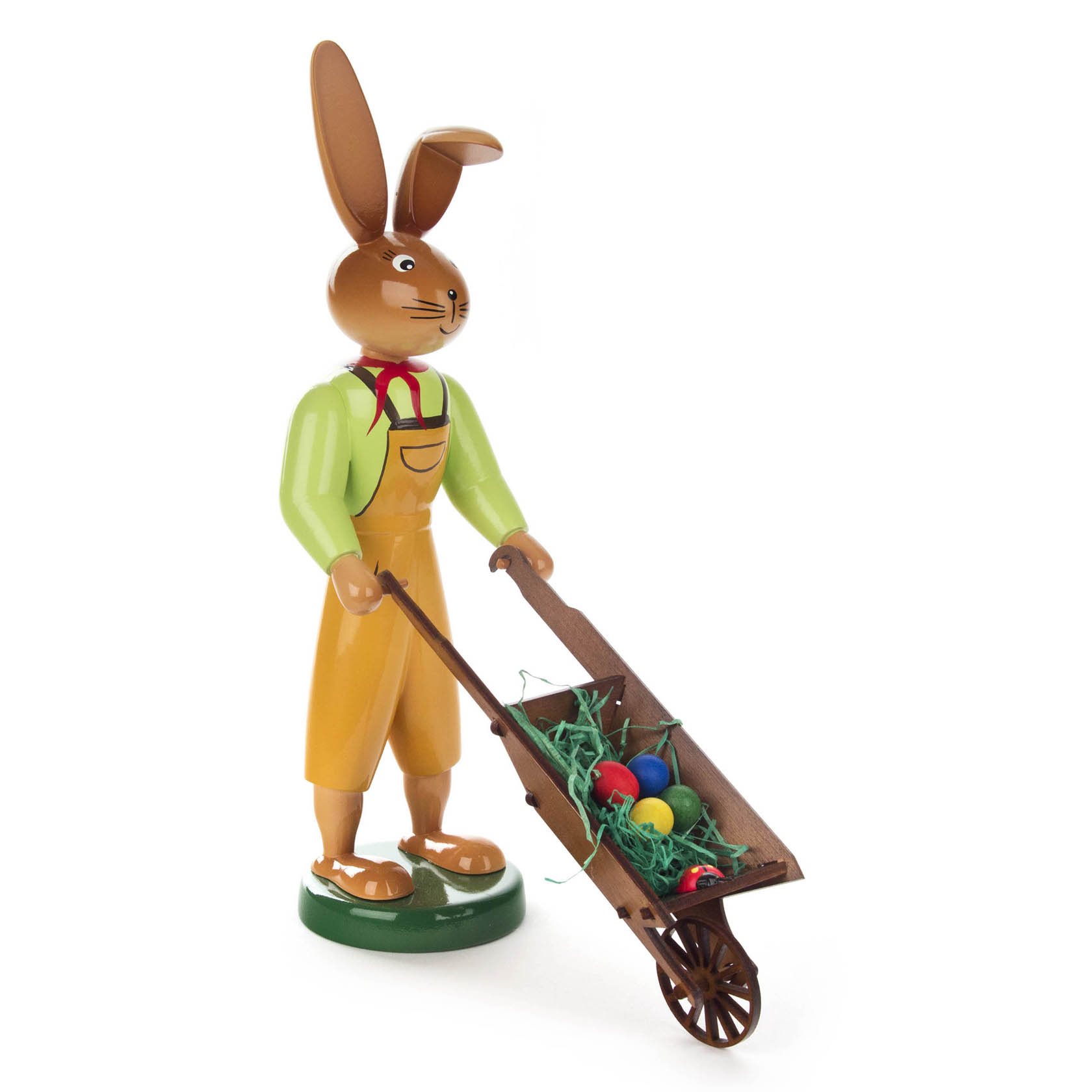 Holzfigur eines Hasen in gelbem Overall und rotem Halstuch, der eine Schubkarre mit bunten Eiern und grüner Deko schiebt. im Dregeno Online Shop günstig kaufen