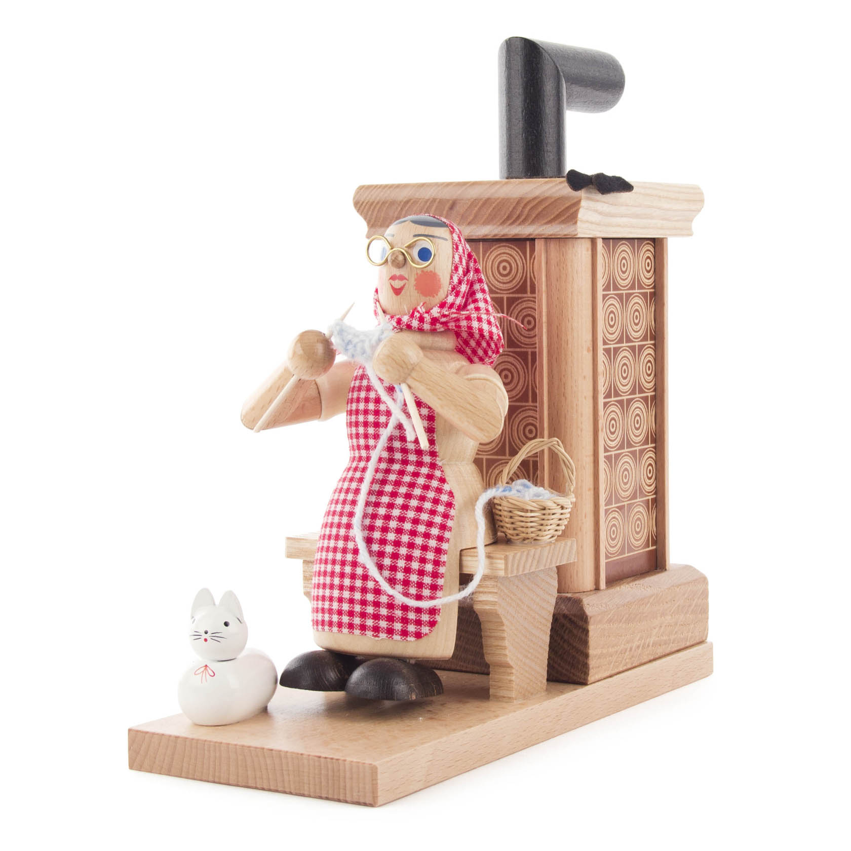 Holzfigur einer älteren Frau mit rotem Kopftuch und Schürze, die strickt, sitzt auf einer Bank neben einem holzgeschnitzten Räucherofen. Eine Katze sitzt auf dem Boden. im Dregeno Online Shop günstig kaufen