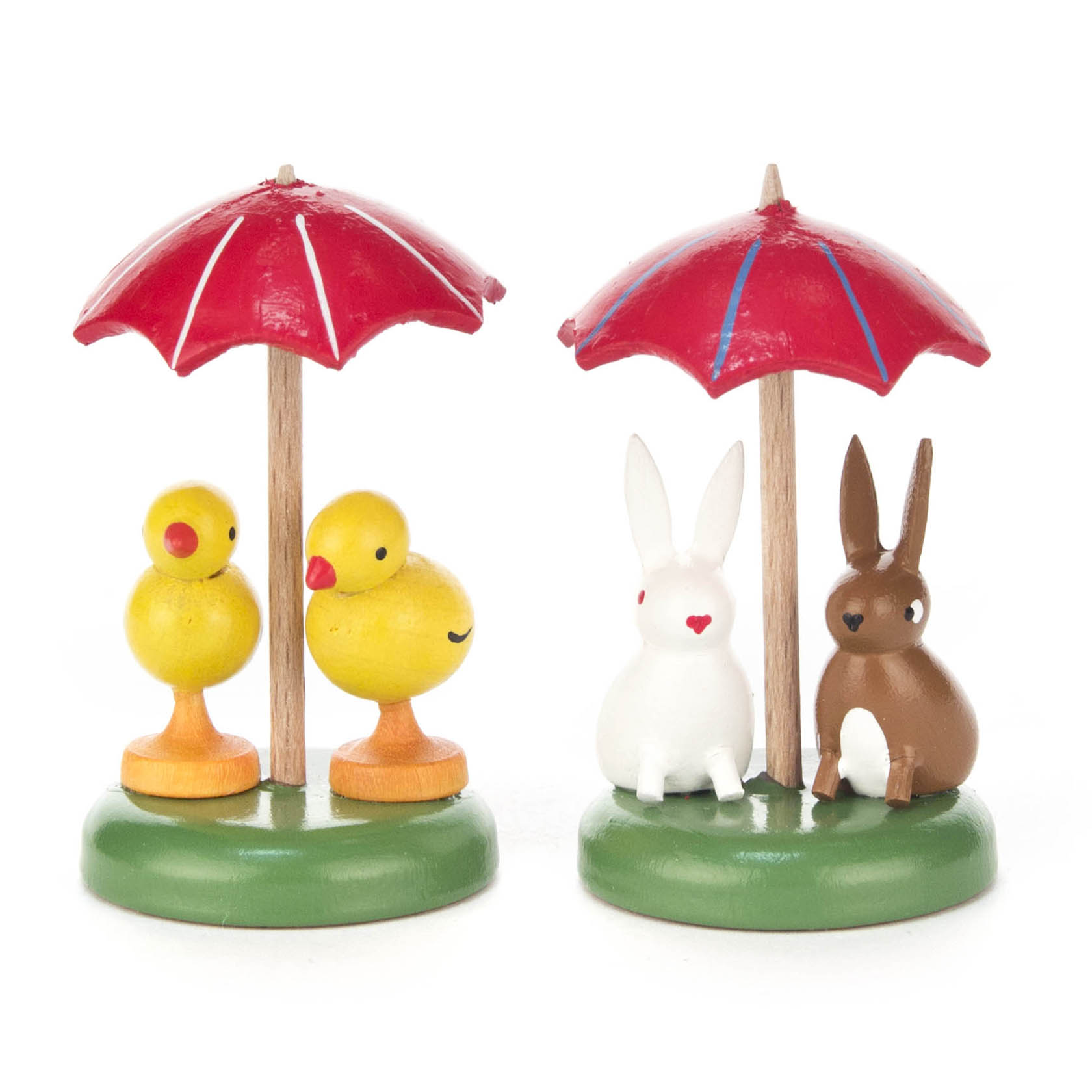 Zwei Holzdioramen mit roten Schirmen, links zwei gelbe Küken und rechts zwei Hasen, ein weißer und ein brauner, alle auf grünem Sockel. im Dregeno Online Shop günstig kaufen