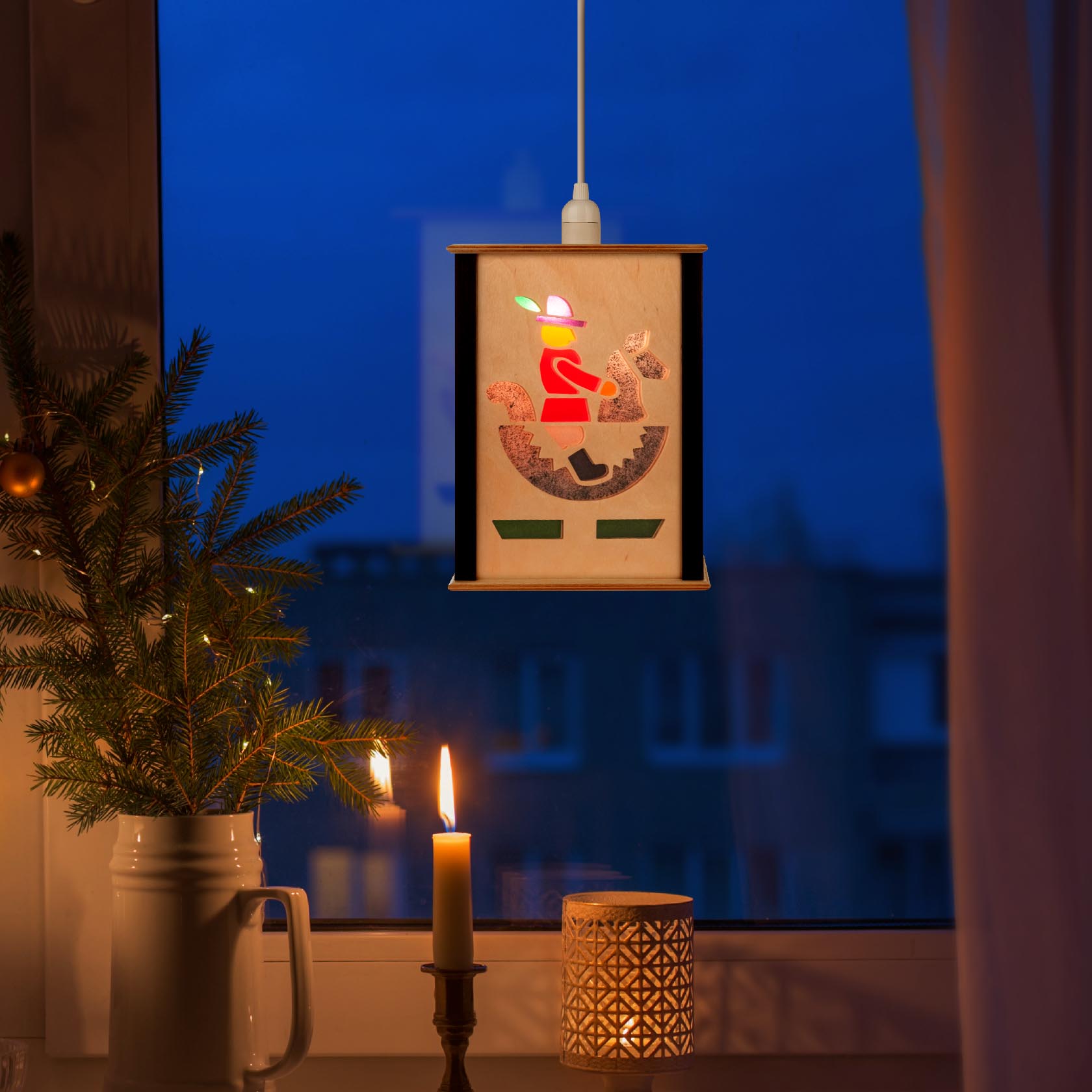 Eine Fensterlaterne mit der Silhouette eines Reiters, die in gemütlicher Dämmerung neben einer Kerze auf einem Fensterbrett hängt.