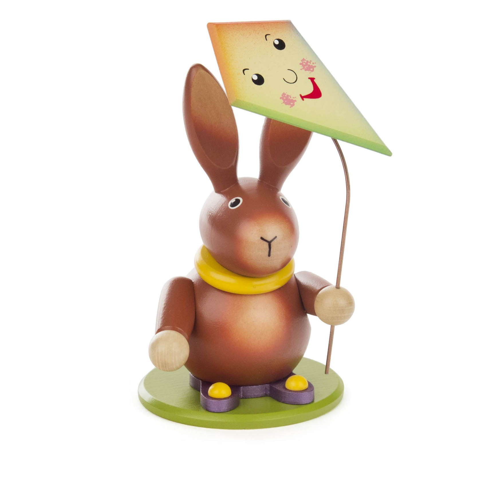 Holzfigur eines lachenden Hasen mit einem bunten Drachen in der Pfote. Der Hase trägt einen gelben Schal und steht auf einer grünen Basis. im Dregeno Online Shop günstig kaufen