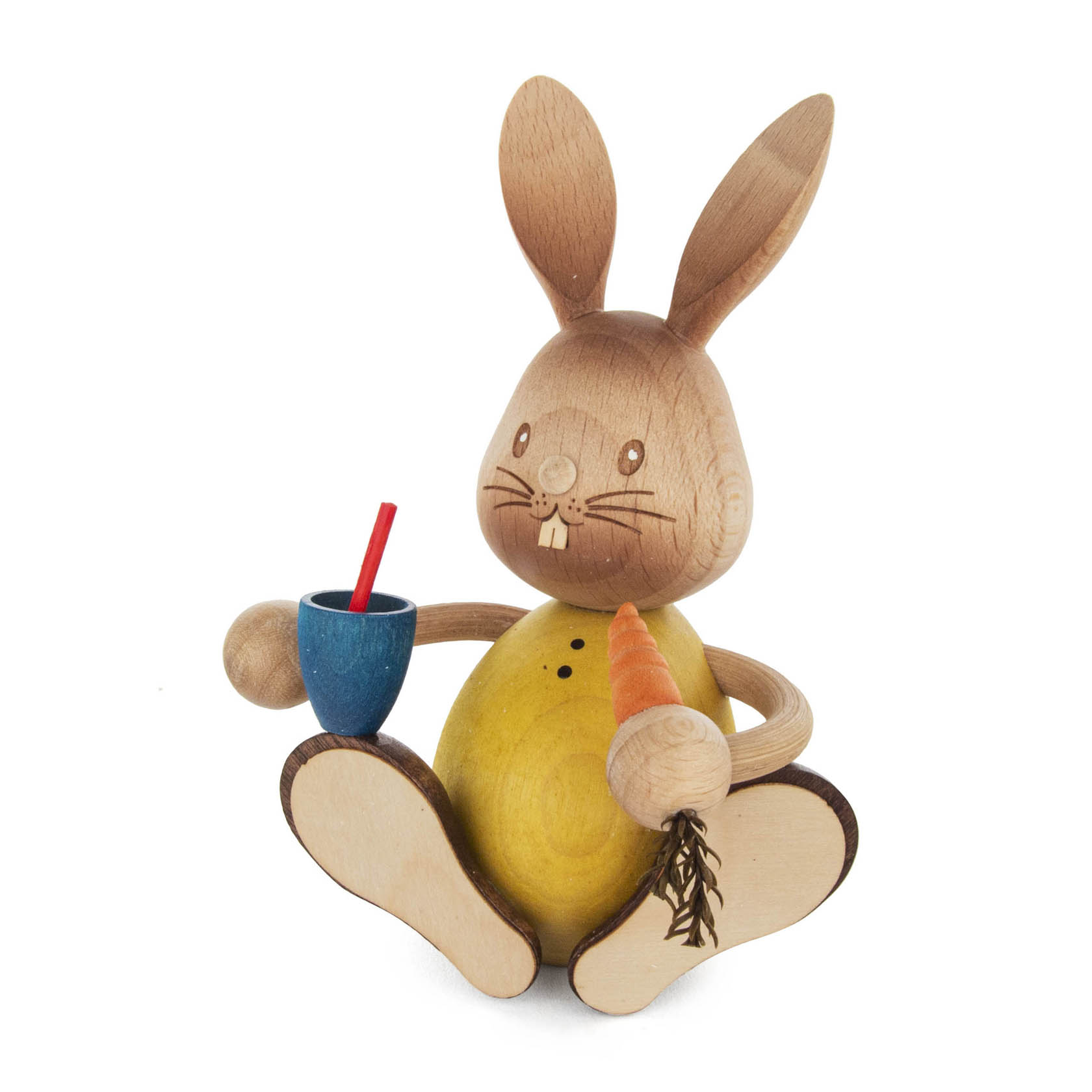 Holzhase Stupsi mit gelbem Bauch hält in der einen Hand eine orange Möhre und in der anderen einen blauen Becher mit Strohhalm. im Dregeno Online Shop günstig kaufen