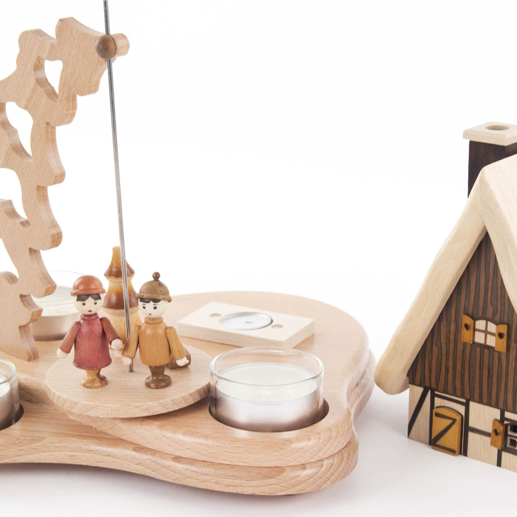 Wooden pyramid with two small figures on a rotating platform, surrounded by spaces for tealight candles, next to a wooden house-shaped incense holder.