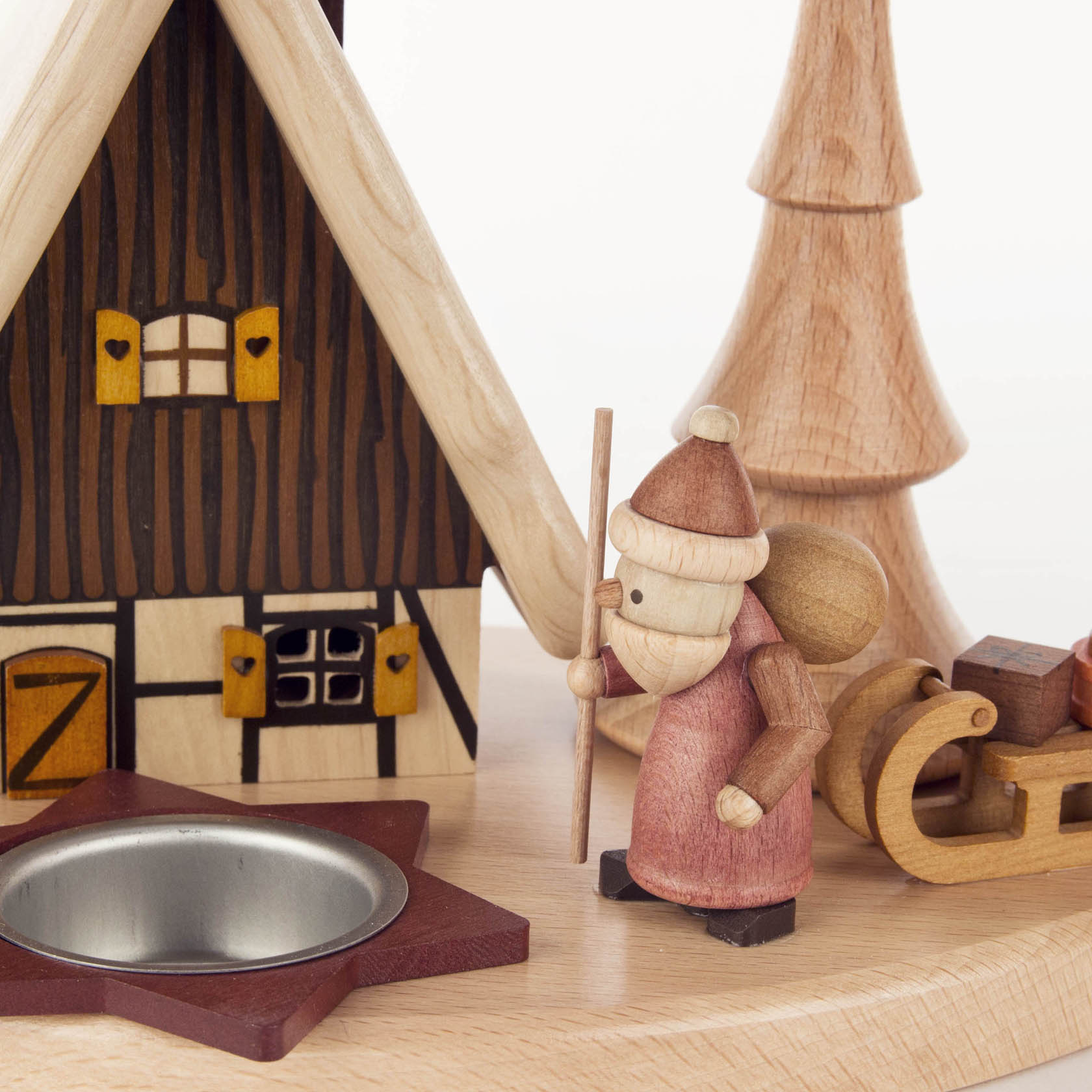 Holz-Schwibbogen mit einem detailreichen Räucherhaus, davor steht eine kleine Holzfigur eines Wanderers mit Stock und Rucksack neben einem Schlitten.