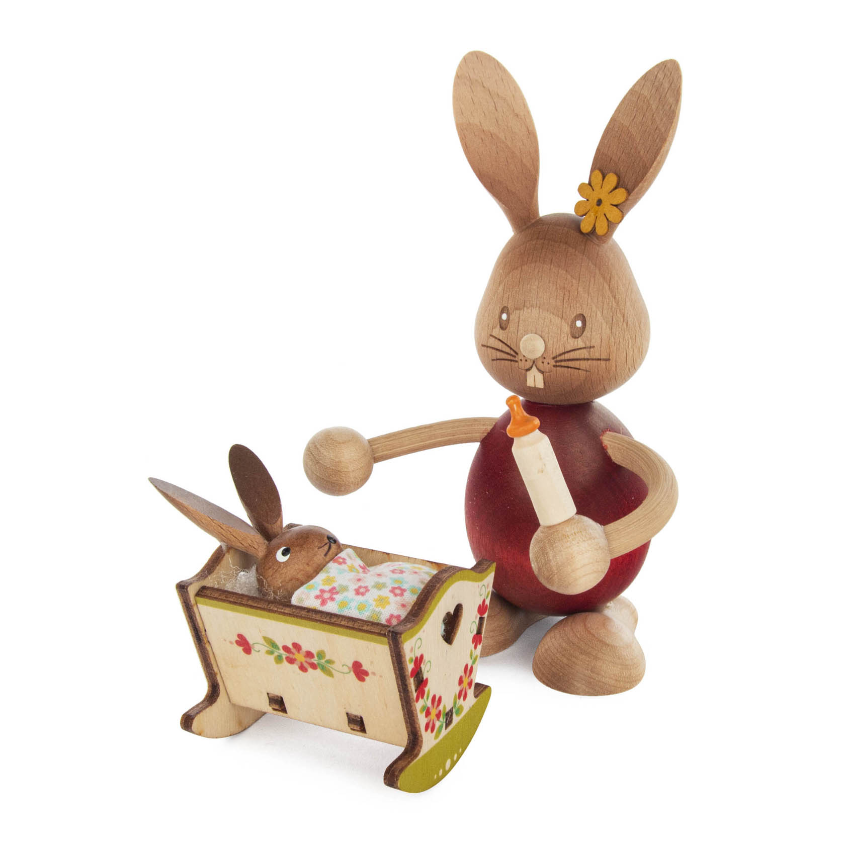 Holzfigur eines stehenden Hasen namens Stupsi mit einer Blume am Ohr, hält eine Babyflasche und steht neben einer kleinen Wiege mit einem Hasenbaby darin. im Dregeno Online Shop günstig kaufen