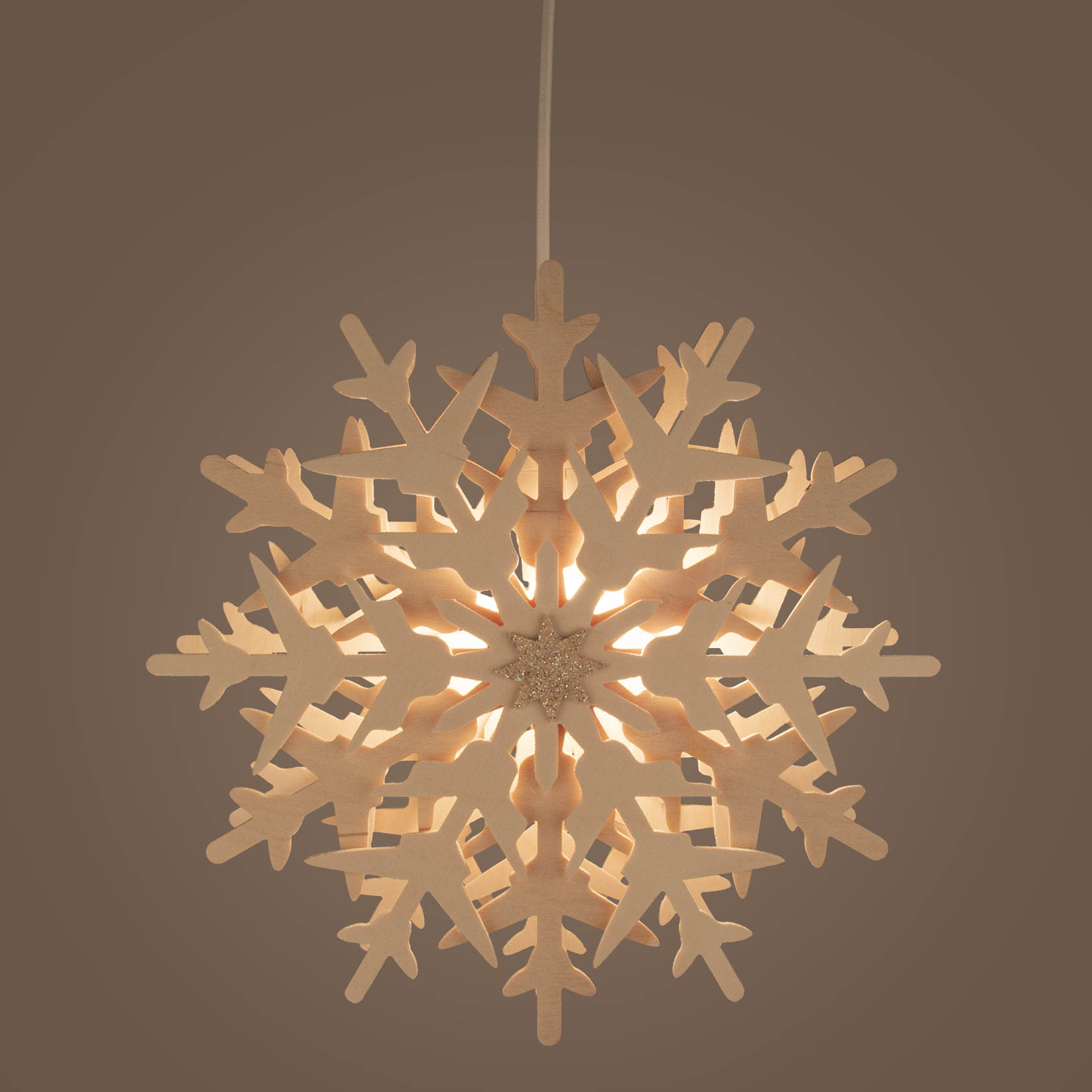 Illuminated snowflake window decoration with intricate cut-out design, glowing softly with electric lighting.