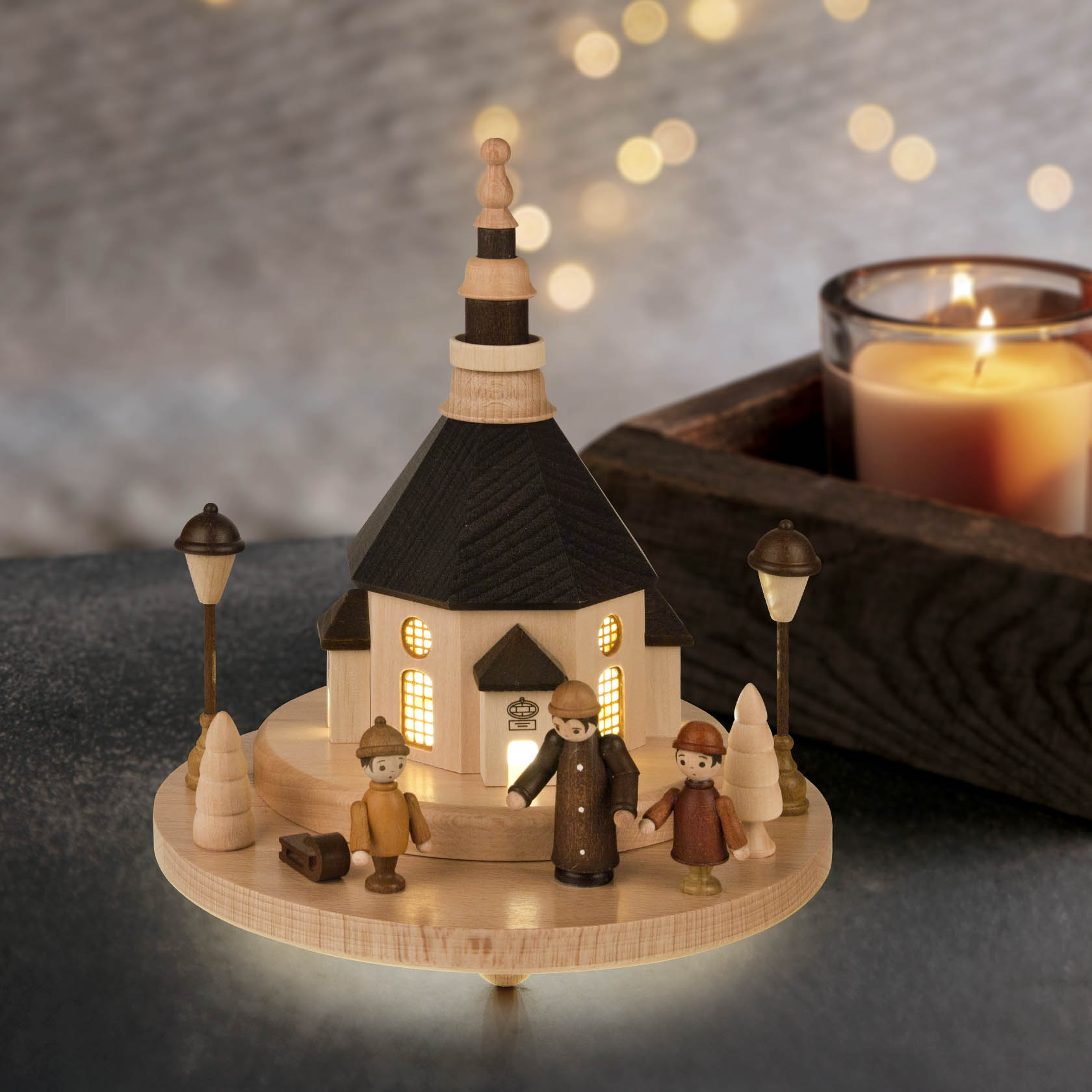 Holzmodel der Seiffener Kirche mit beleuchteten Fenstern und drei Marktfiguren: ein Mann und zwei Kinder. LED Beleuchtung und Straßenlaternen.