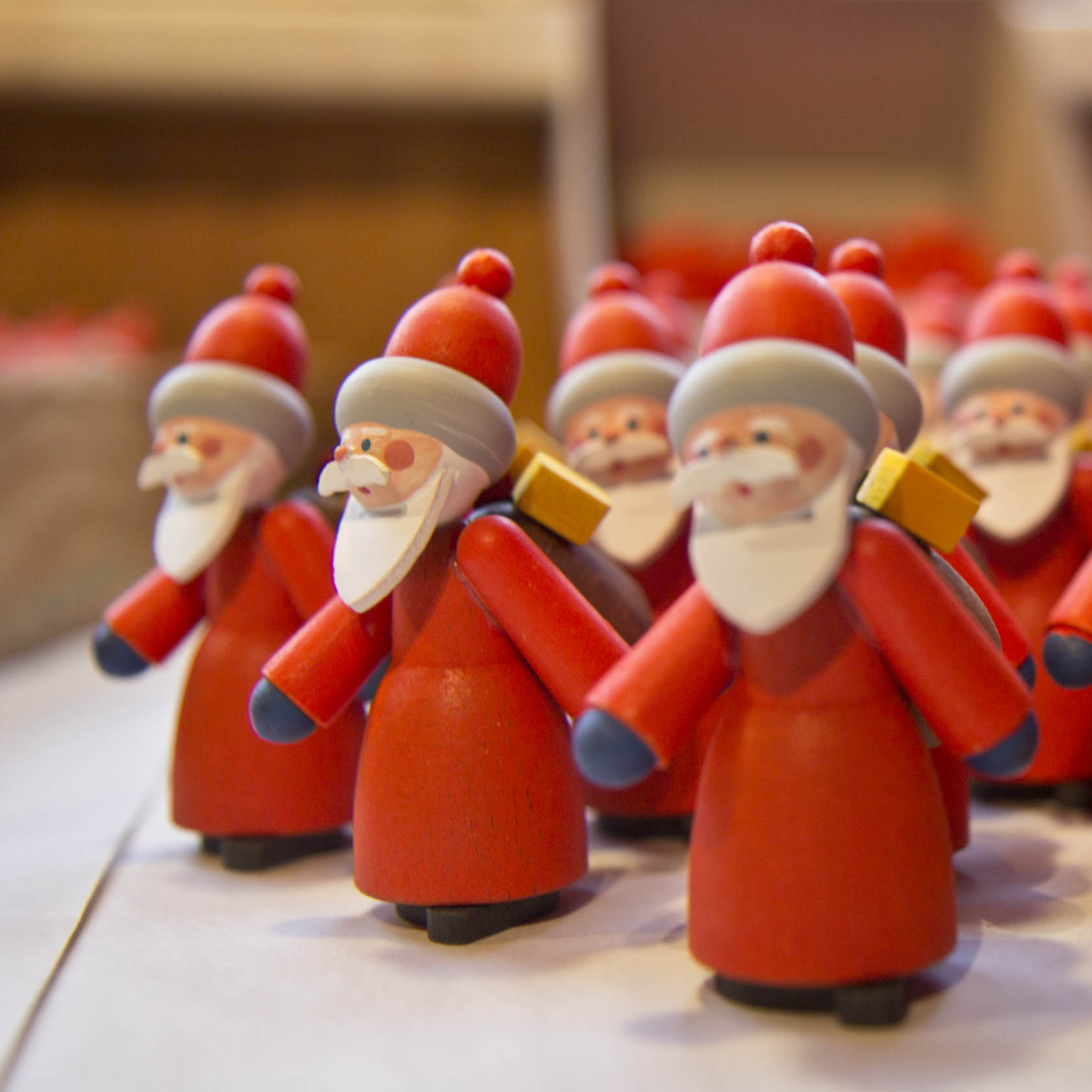Nahaufnahme von mehreren kleinen, holzgeschnitzten Weihnachtsmannfiguren in rotem Gewand und mit weißem Bart, die nebeneinander aufgestellt sind.