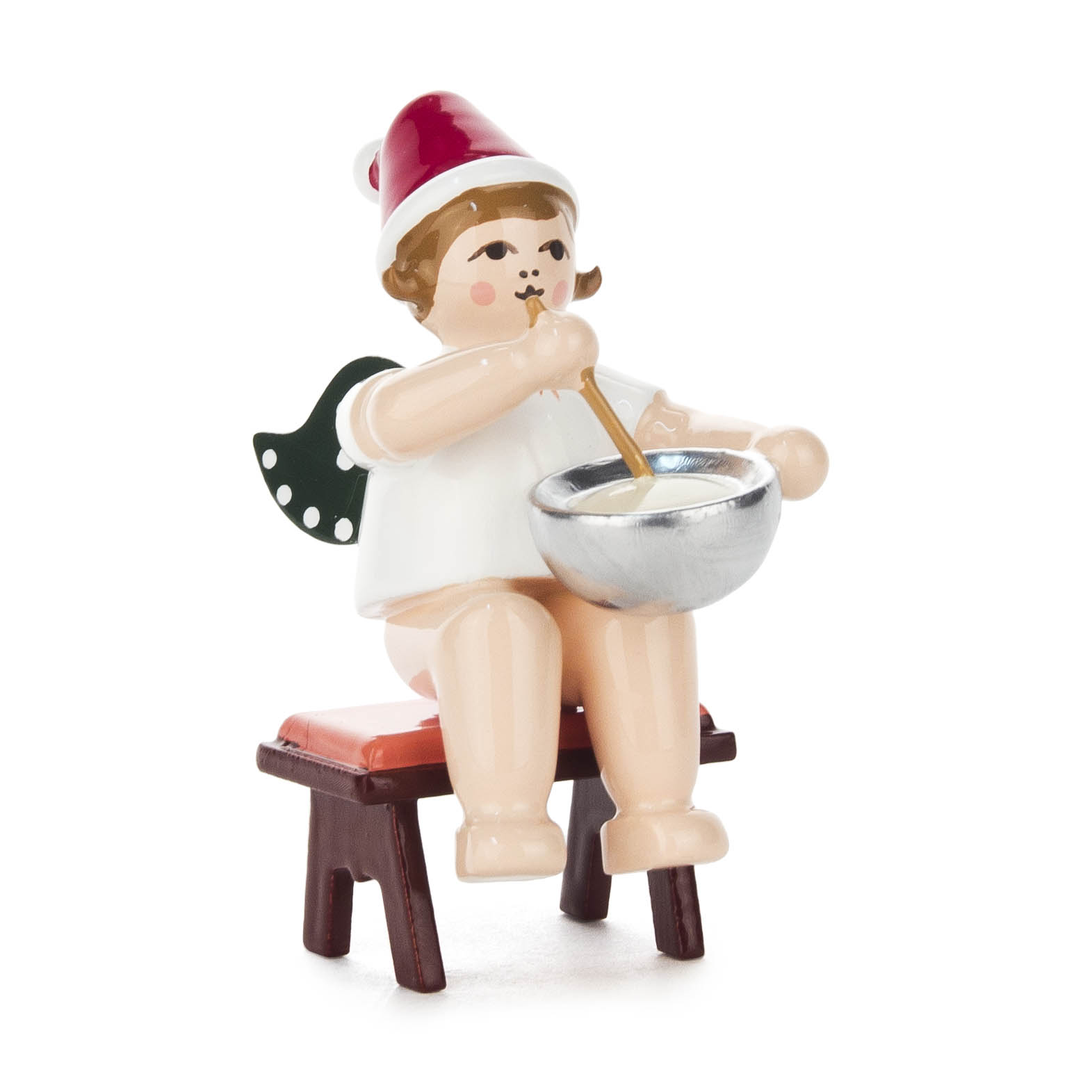 Eine sitzende Engelsfigur mit grünen Flügeln und roter Mütze, die eine silberne Teigschüssel hält und rührt. Der Engel sitzt auf einem kleinen Hocker. im Dregeno Online Shop günstig kaufen