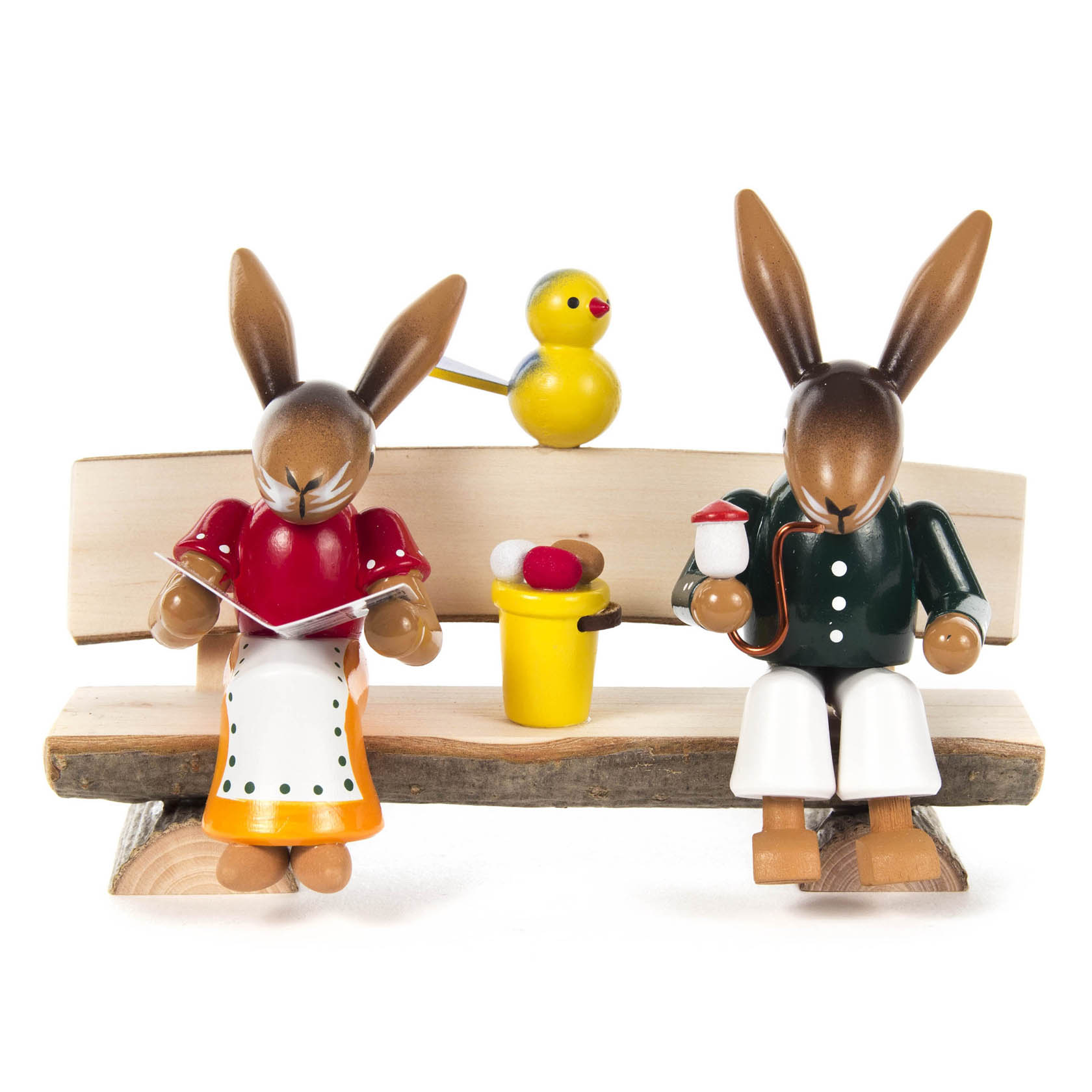 Zwei Holzhasenfiguren sitzen auf einer Bank. Ein Hase liest ein Buch, der andere hält eine Tasse. Ein gelbes Küken sitzt in der Mitte. im Dregeno Online Shop günstig kaufen