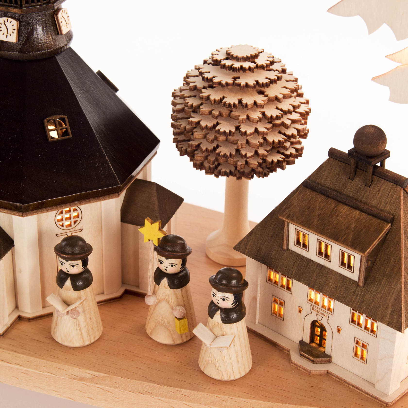Elektrisch beleuchteter Schwibbogen mit Seiffener Kirche, Holzhäusern und Kurrendefiguren in traditioneller Tracht vor einem holzgeschnitzten Baum.