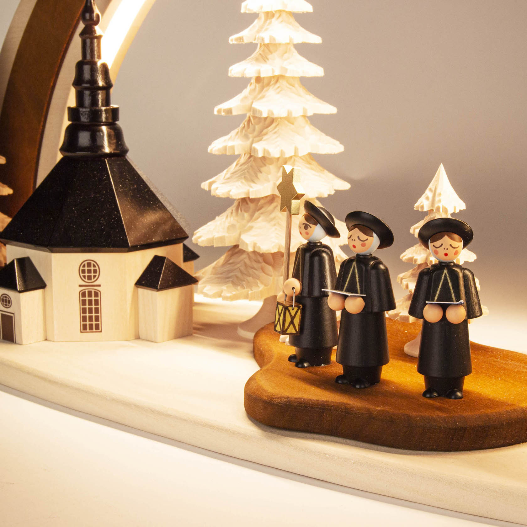 Massivholzbogen der Seiffener Kirche mit drei Kurrende-Sängern in traditioneller Kleidung und LED-Beleuchtung, vor einem Holzbaumhintergrund.