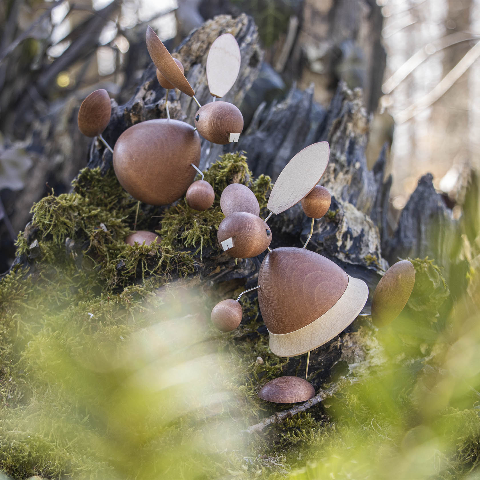 Zwei hölzerne Hasenfiguren mit großen Ohren und weißen Zähnen sitzen auf einem mit Moos bedeckten Baumstumpf.