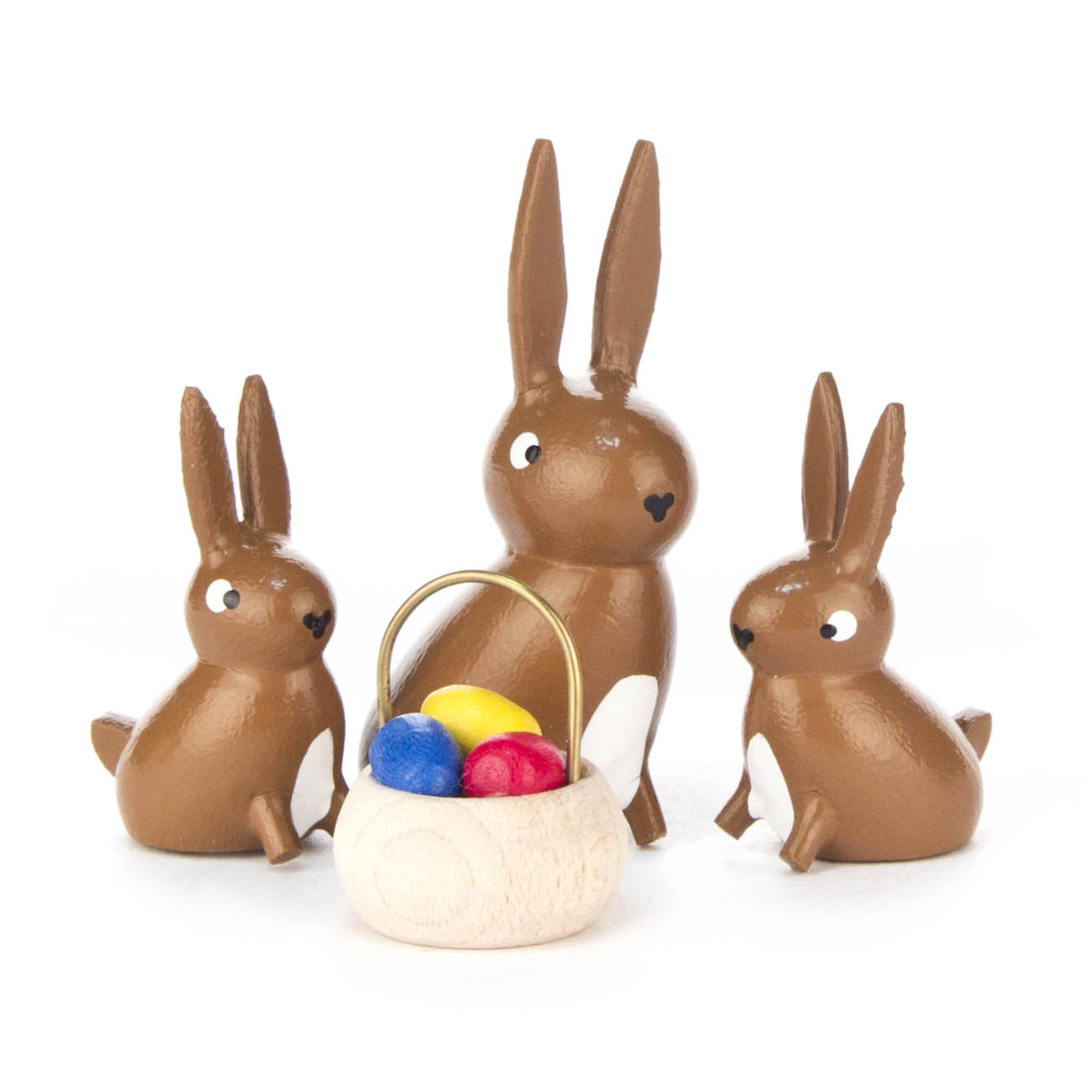 Drei holzgeschnitzte Hasenfiguren, ein großer und zwei kleine, umgeben ein kleines Körbchen mit bunten Eiern. im Dregeno Online Shop günstig kaufen