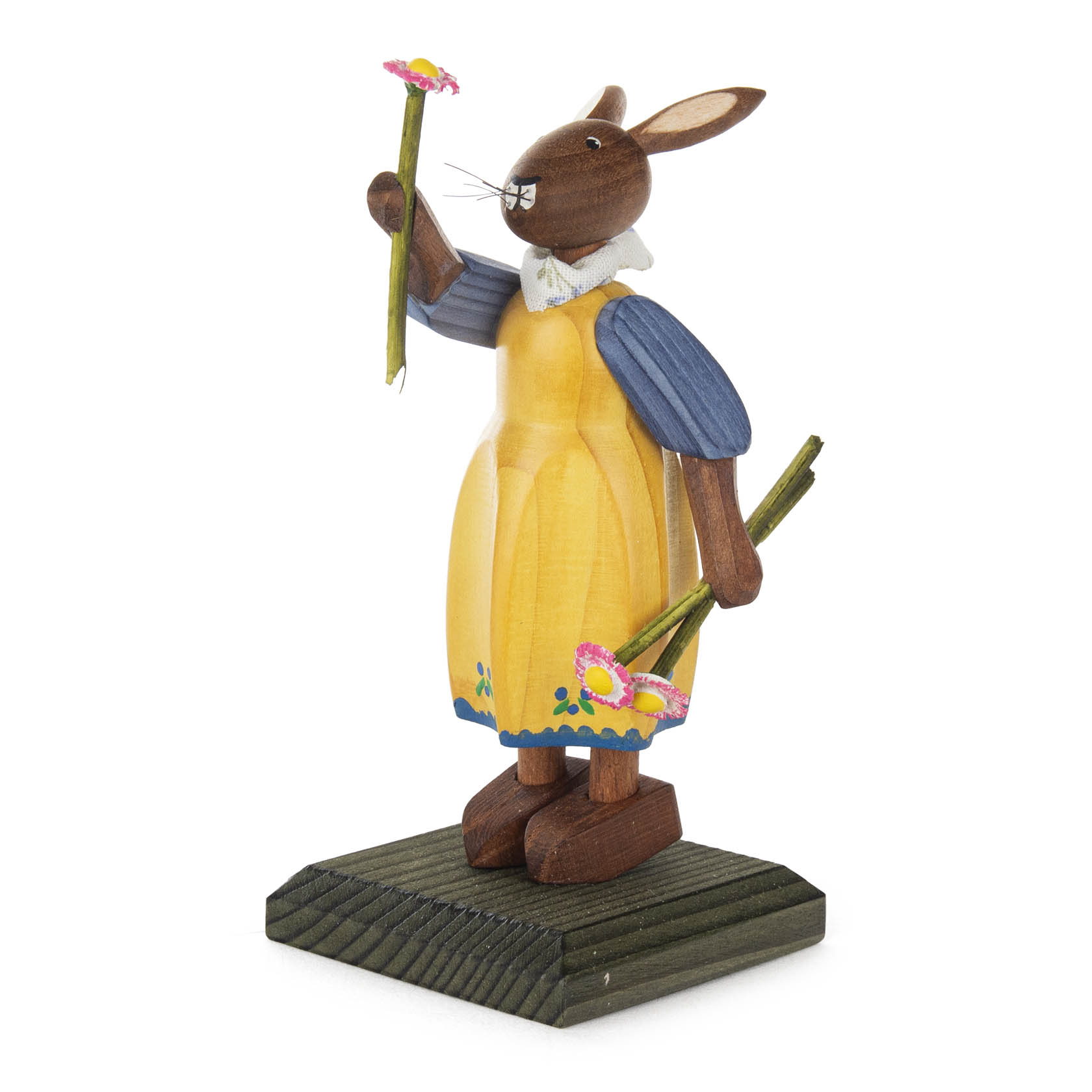 Holzfigur eines Hasenmädchens in einem gelben Kleid mit blauen Ärmeln, das zwei bunte Blumen in den Händen hält, auf einem grünen Sockel stehend. im Dregeno Online Shop günstig kaufen