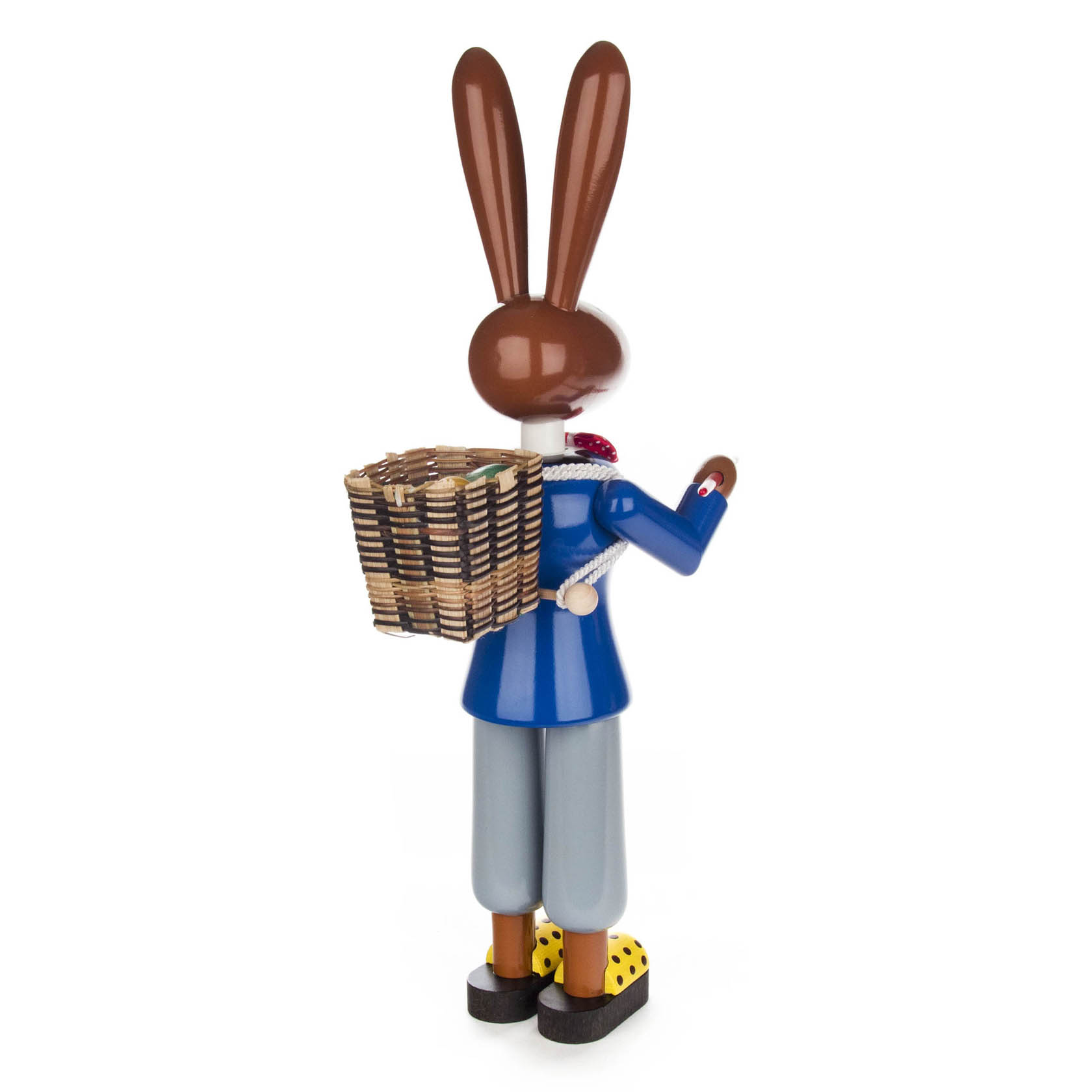 Holzfigur eines Hasenmannes in blauer Jacke, grauen Hosen und gelben Holzschuhen mit schwarzen Punkten. Er trägt einen Korb auf dem Rücken.