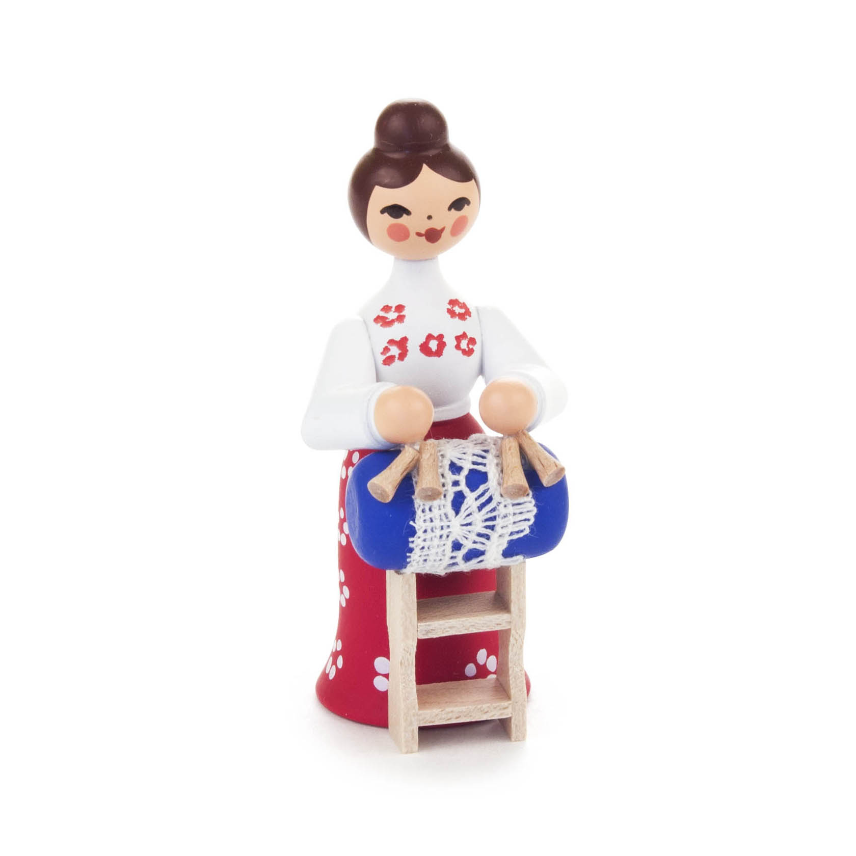 Holzfigur einer Frau mit braunem Haar, in rotem Kleid mit weißen Blumen. Sie hält ein blaues Kissen mit Spitzenklöppeln und steht hinter einem Klöppelschnitt. im Dregeno Online Shop günstig kaufen