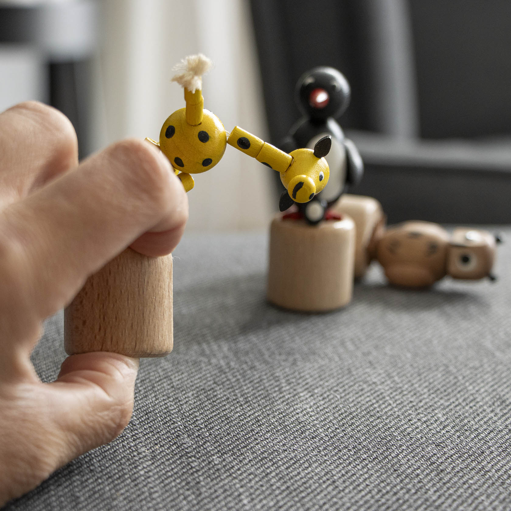 Eine Hand drückt auf den Sockel einer gelben Wackeltier-Giraffe mit schwarzen Flecken, wodurch die Giraffe in Bewegung gerät.