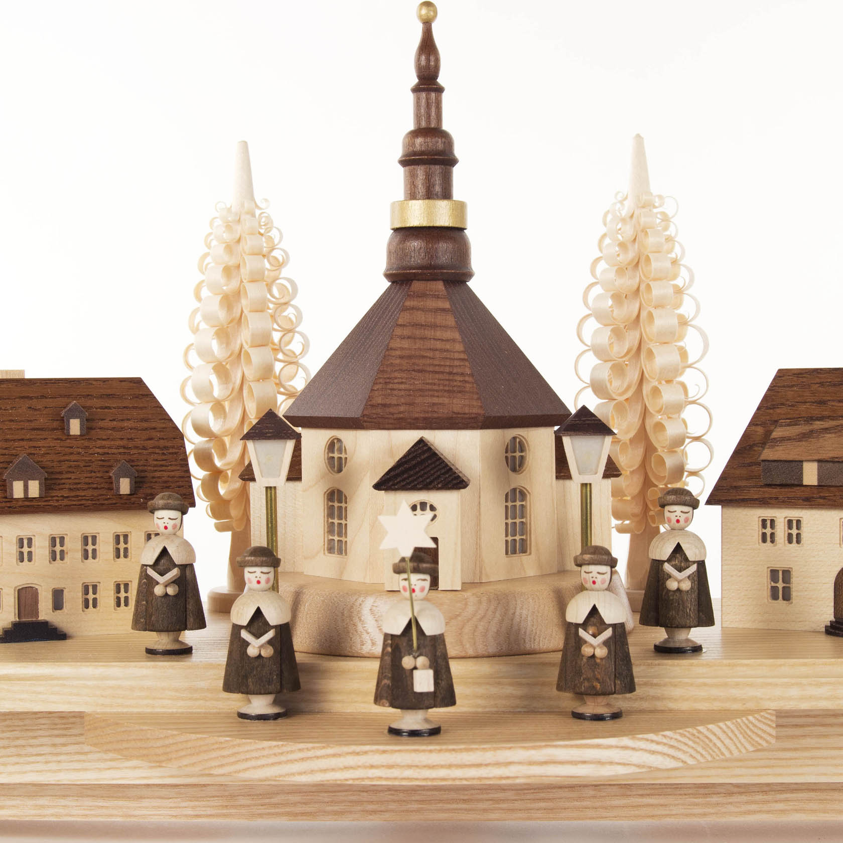 Ein Schwibbogen mit einer Seiffener Kirche in der Mitte, flankiert von zwei großen Holzspiralbäumen. Davor stehen sechs Kurrende-Sänger in traditioneller Kleidung.