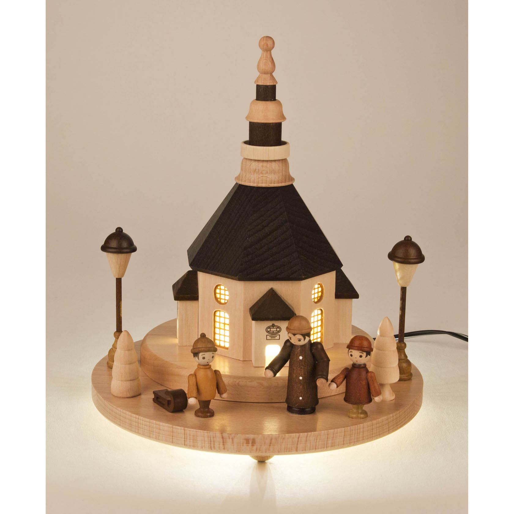 Holzmodell einer Seiffener Kirche auf einem Sockel, umgeben von drei Marktfiguren und Straßenlaternen, beleuchtet von LEDs.