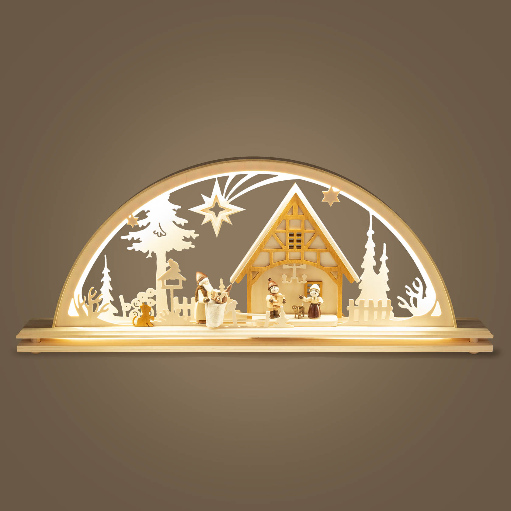 Ein Schwibbogen zeigt eine weihnachtliche Szene mit einem beleuchteten Holzhaus, drei Figuren und Weihnachtsdekoration, darunter ein Stern und Bäume.