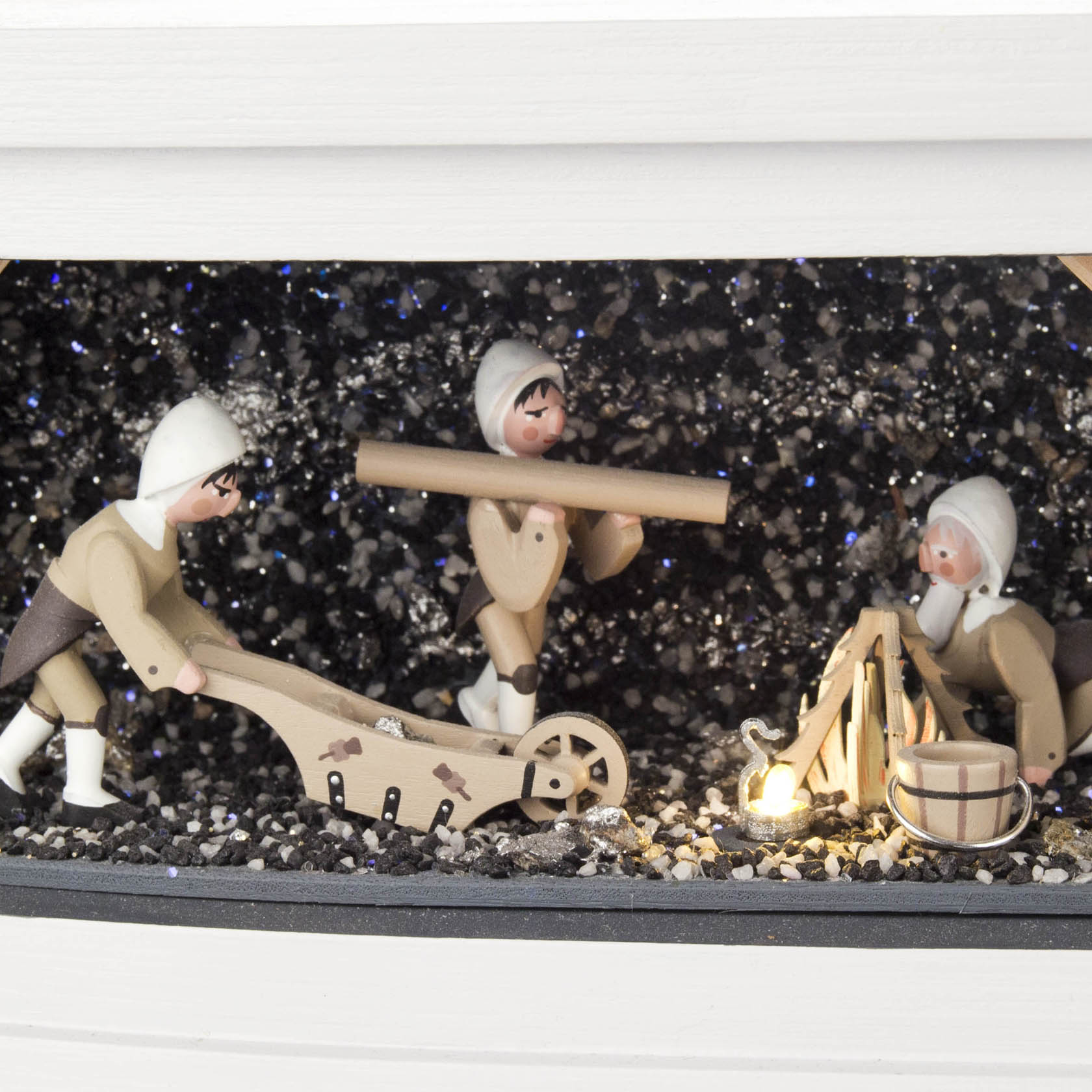 Drei Holzfiguren in traditioneller Bergmannskleidung: Einer zieht einen Schlitten, einer trägt schweres Werkzeug, und einer sitzt am Lagerfeuer.