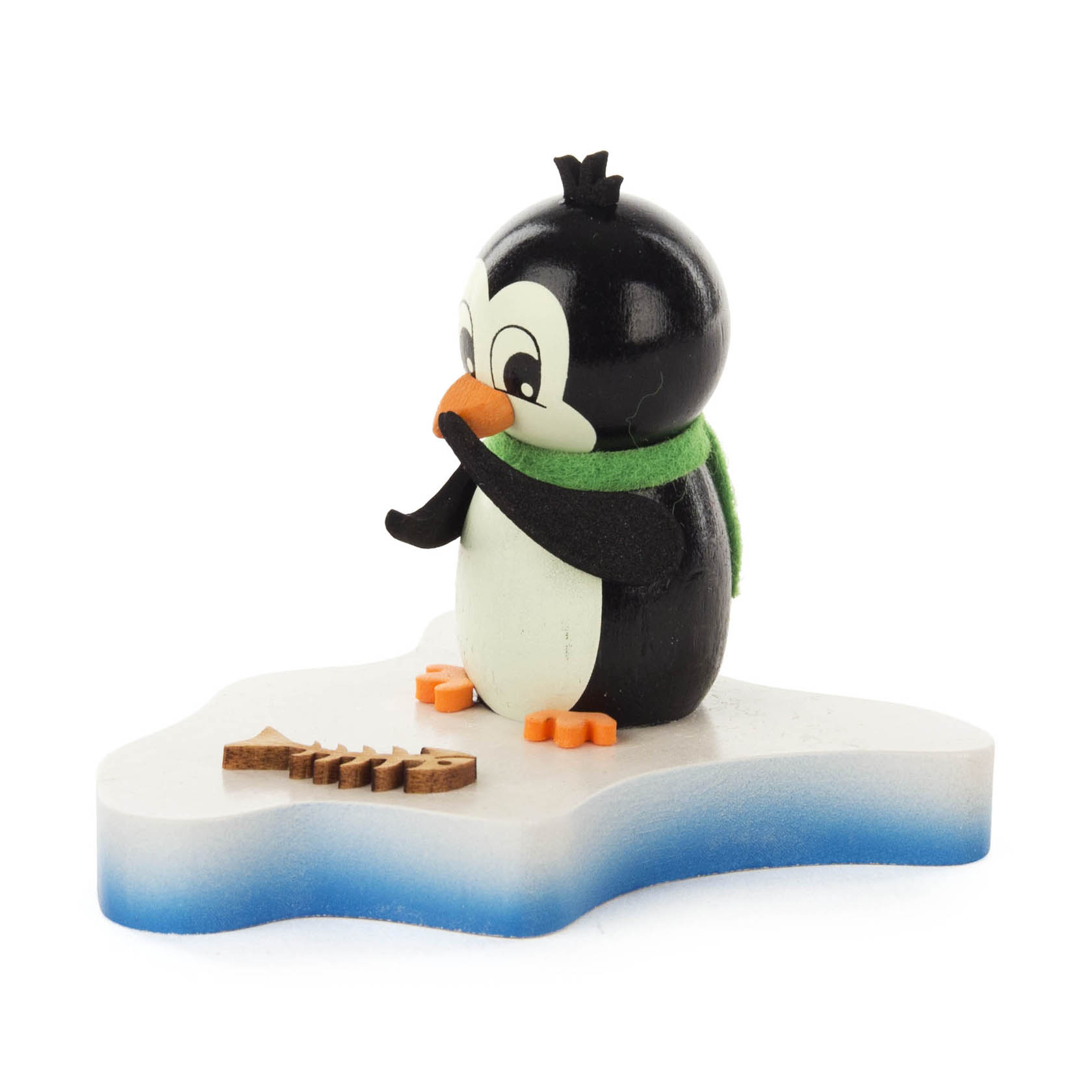 Ein lächelnder Pinguin mit grünem Schal sitzt auf einer Eisfläche und betrachtet neugierig einen kleinen Holzfisch vor sich. im Dregeno Online Shop günstig kaufen