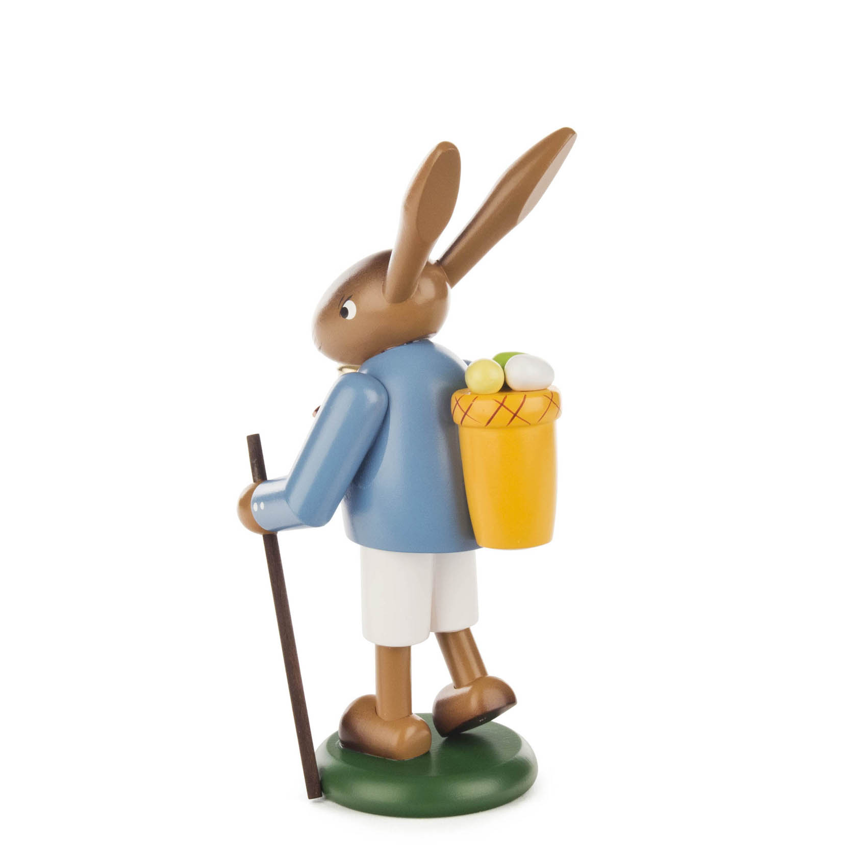 Holzfigur eines stehenden Osterhasen, der einen blauen Mantel und eine weiße Hose trägt. Er hält einen Wanderstock und trägt einen Korb mit Ostereiern.