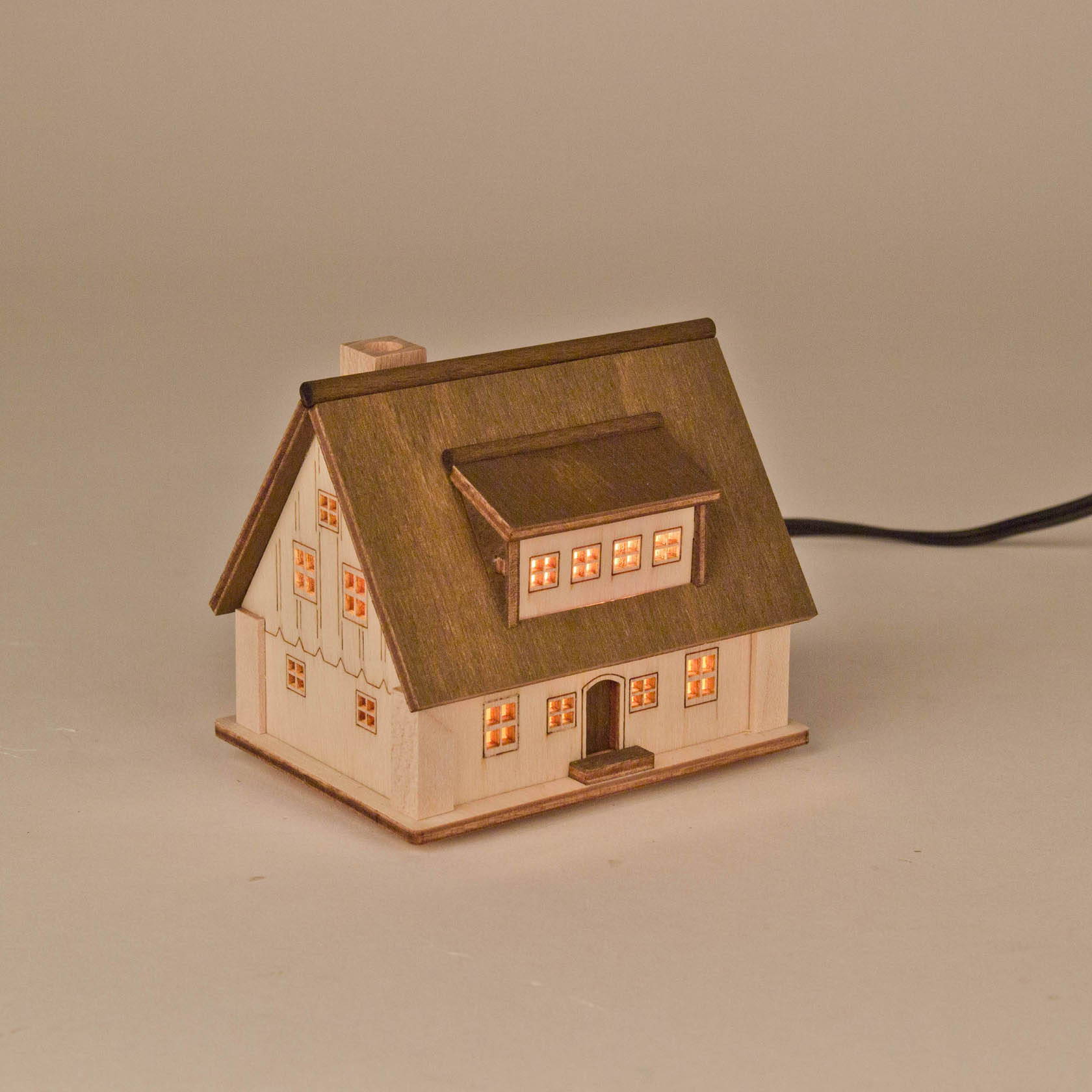 Ein kleines, dekoratives Lichterhaus aus Holz mit beleuchteten Fenstern und einer Tür. Ideal als stimmungsvolle Weihnachtsdeko.