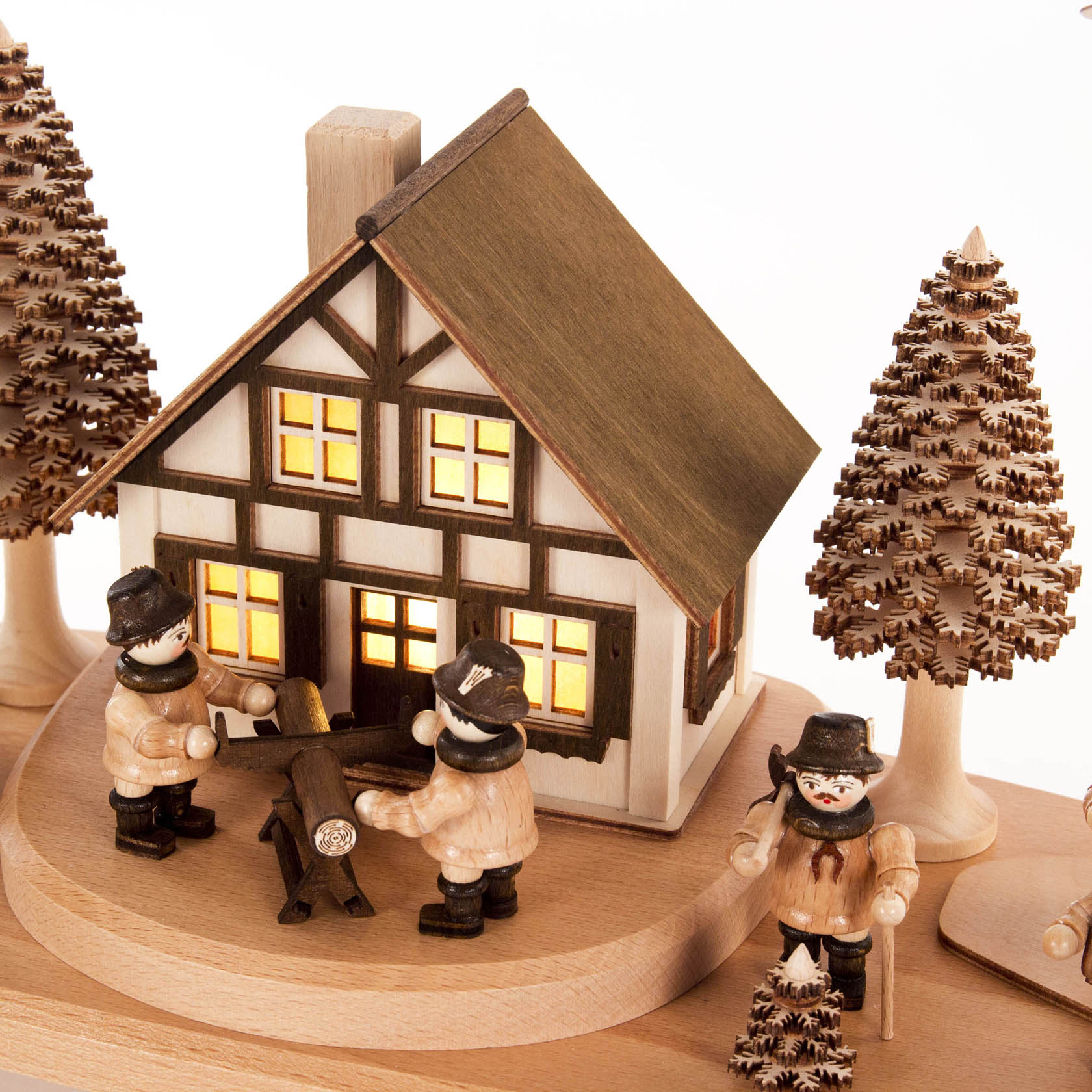 Ein Schwibbogen zeigt ein Forsthaus mit innenbeleuchteten Fenstern, umgeben von zwei Holzfiguren, die Bäume fällen und tragen. Daneben stehen weitere Bäume und Waldleute.