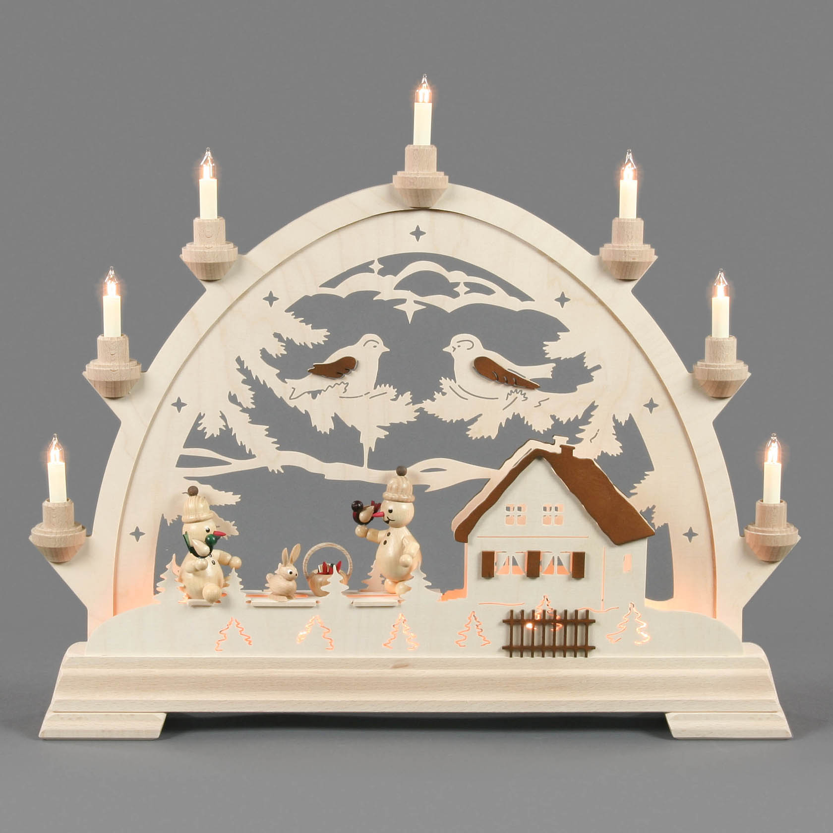 Ein beleuchteter Schwibbogen mit Schneemännern, Kerzen und winterlicher Waldlandschaft mit kleinen Vögeln und einem Häuschen.