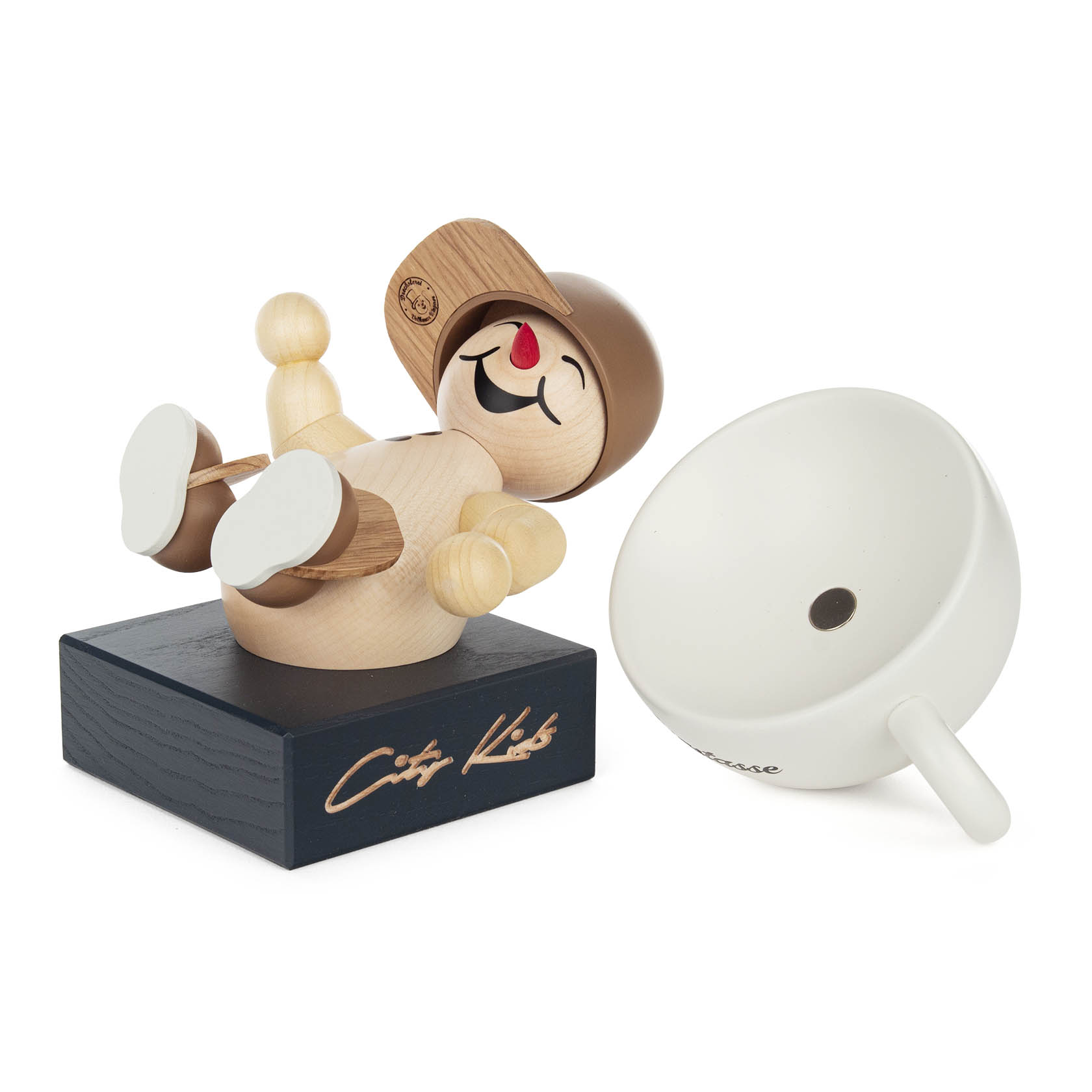 Holzfigur 'City Kids' Elio mit braunen Schuhen und Cappie, auf Rücken liegend. Neben der Figur liegt eine weiße Tasse.