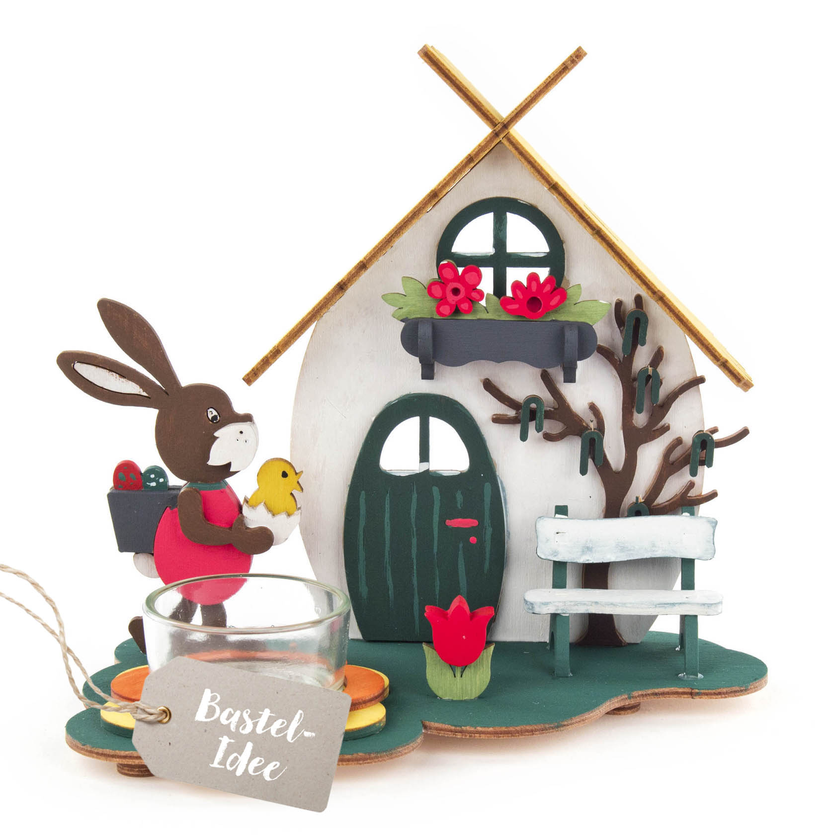 Ein dekorativer Teelichthalter in Form eines Osterhauses mit einem Hasen, der ein Küken trägt. Im Vordergrund ist ein Glas für ein Teelicht. im Dregeno Online Shop günstig kaufen