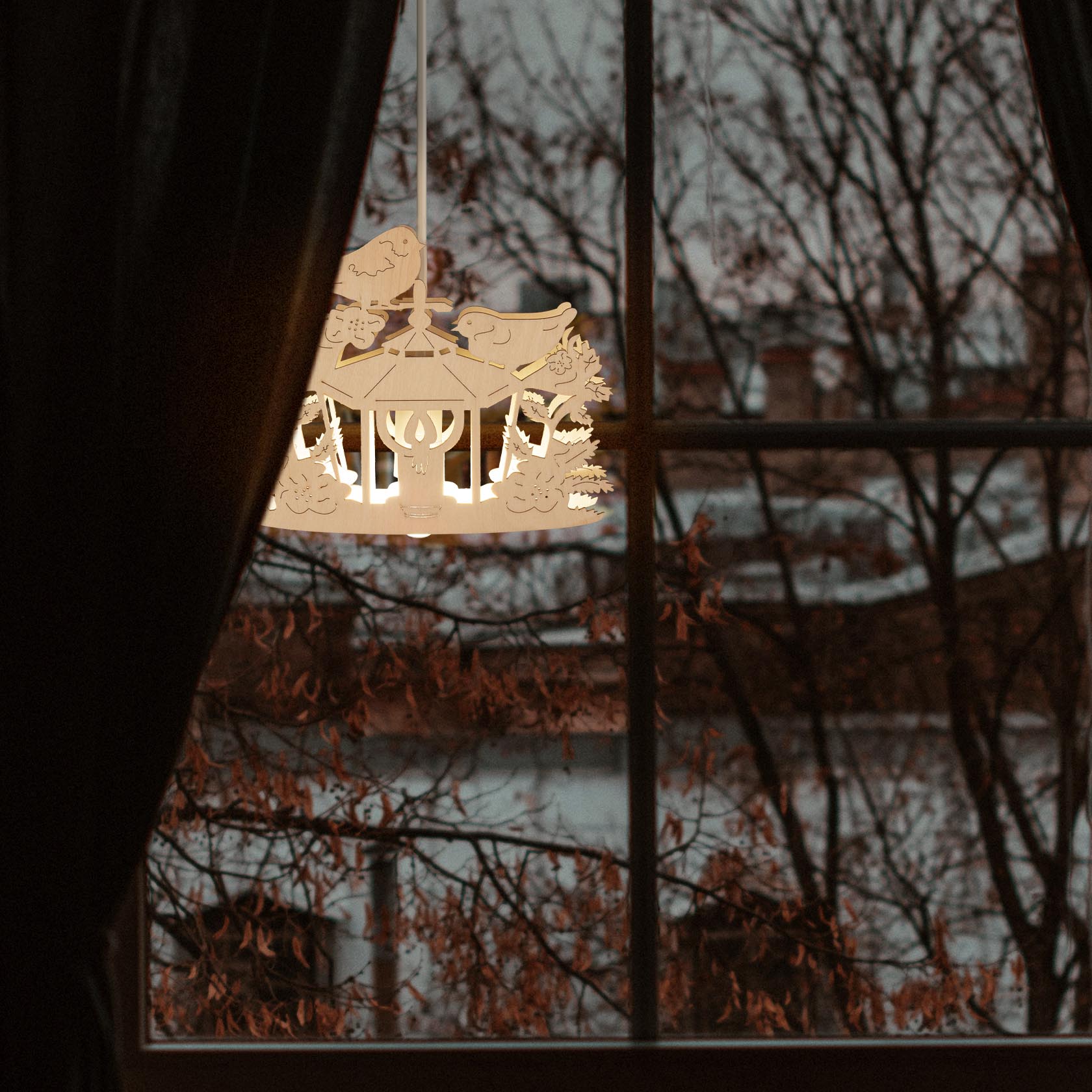 Eine weiße, elektrisch beleuchtete Laterne mit ausgeschnittenen Vogeldesigns, hängt vor einem Fenster. Draußen sind Bäume im Hintergrund erkennbar.
